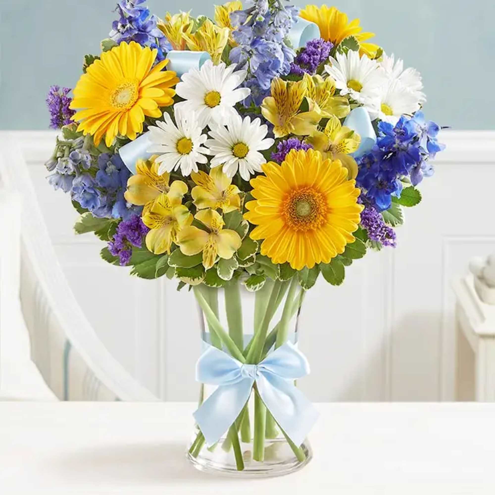 Bouquet of yellow and white daisies with blue and purple flowers in a glass vase