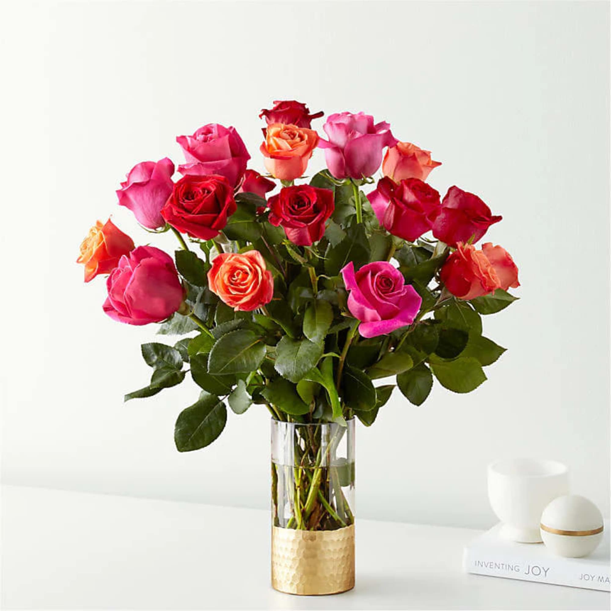Mixed roses in pink, red, and orange arranged in a clear vase