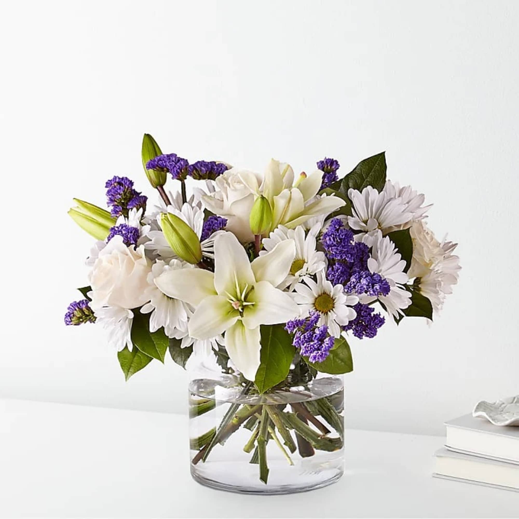 White lilies and daisies with purple filler in a glass vase