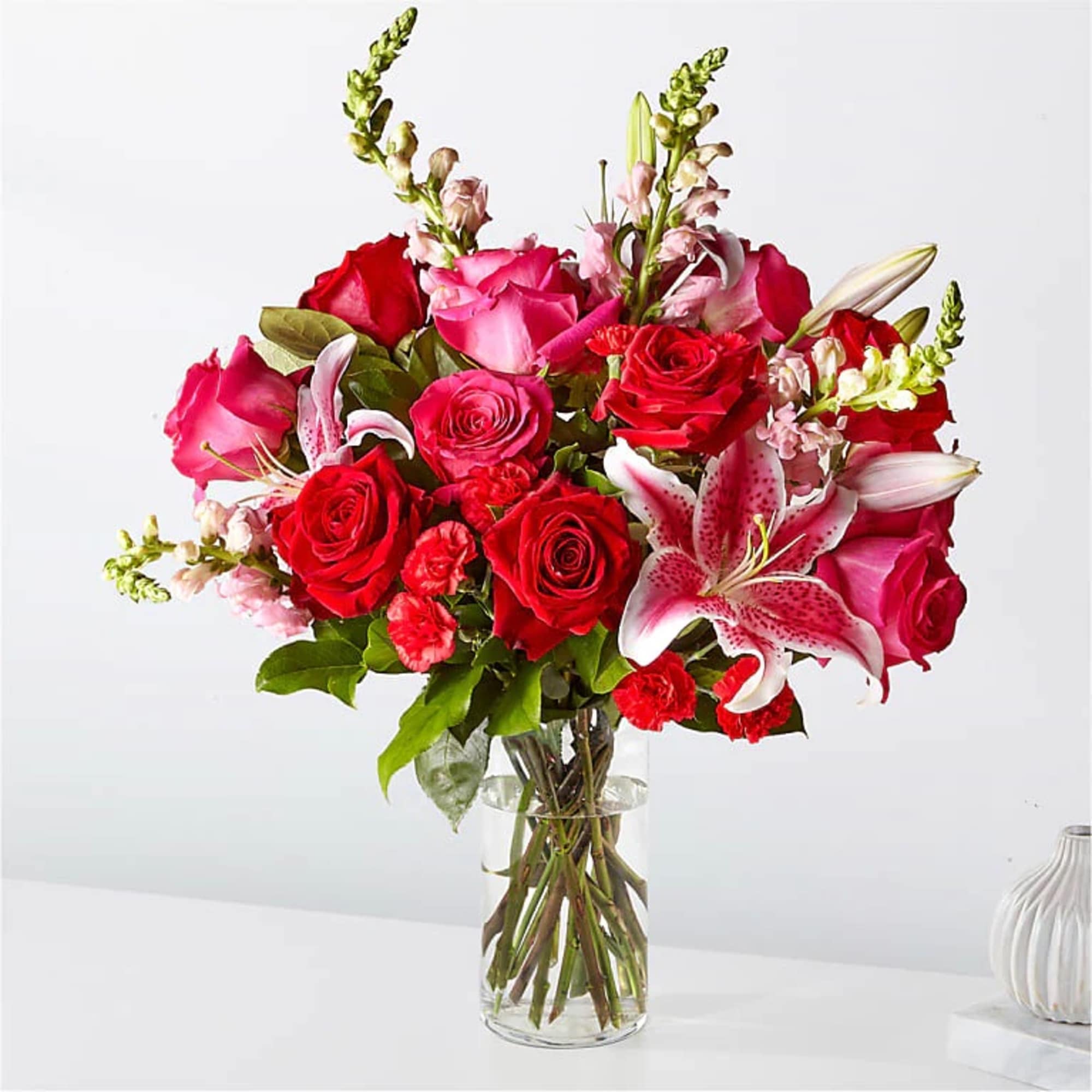 Bouquet of red and pink roses with lilies in a clear glass vase