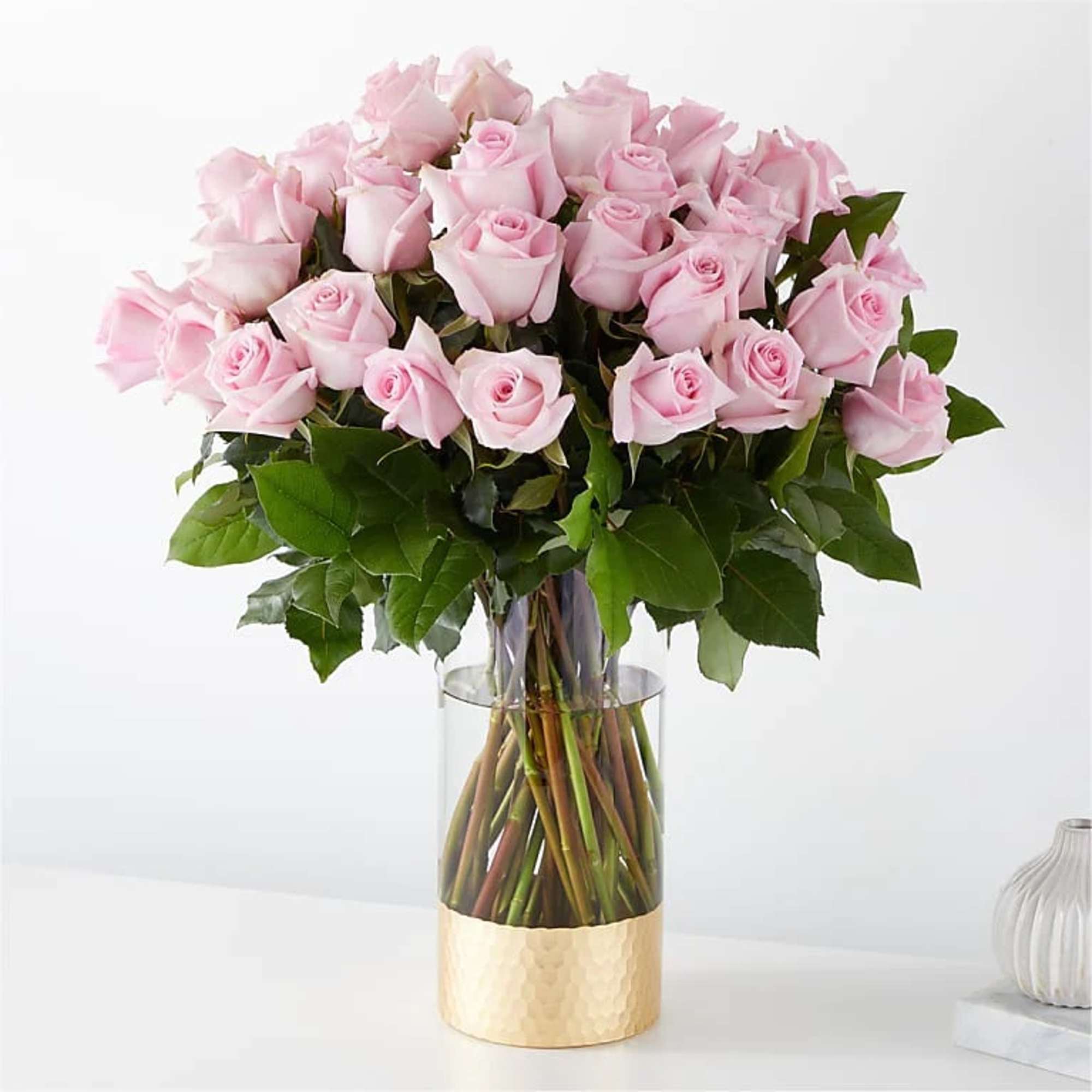Bouquet of pale pink roses in a clear glass vase with a gold base