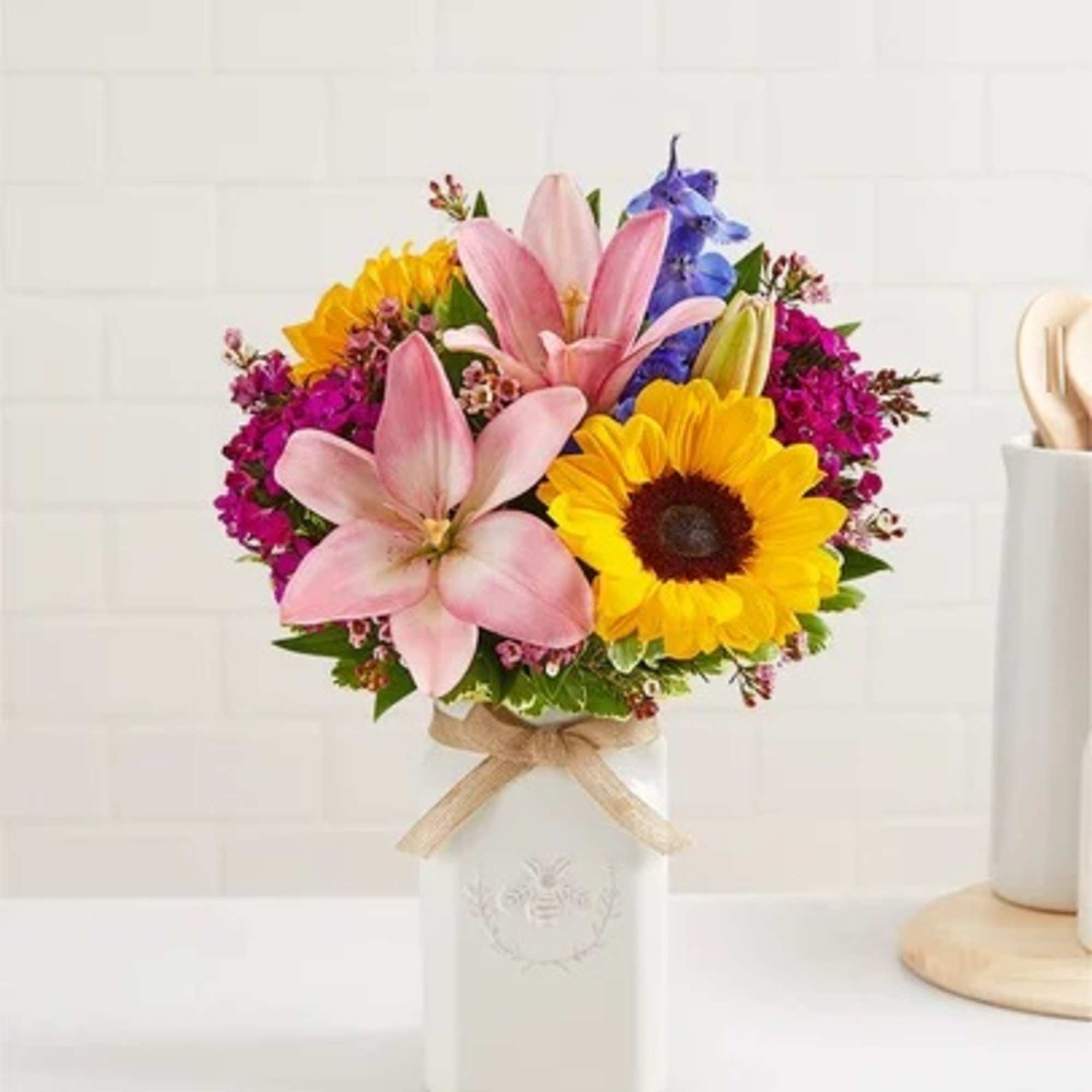 Bouquet of pink lilies, sunflowers, and purple flowers in a white vase
