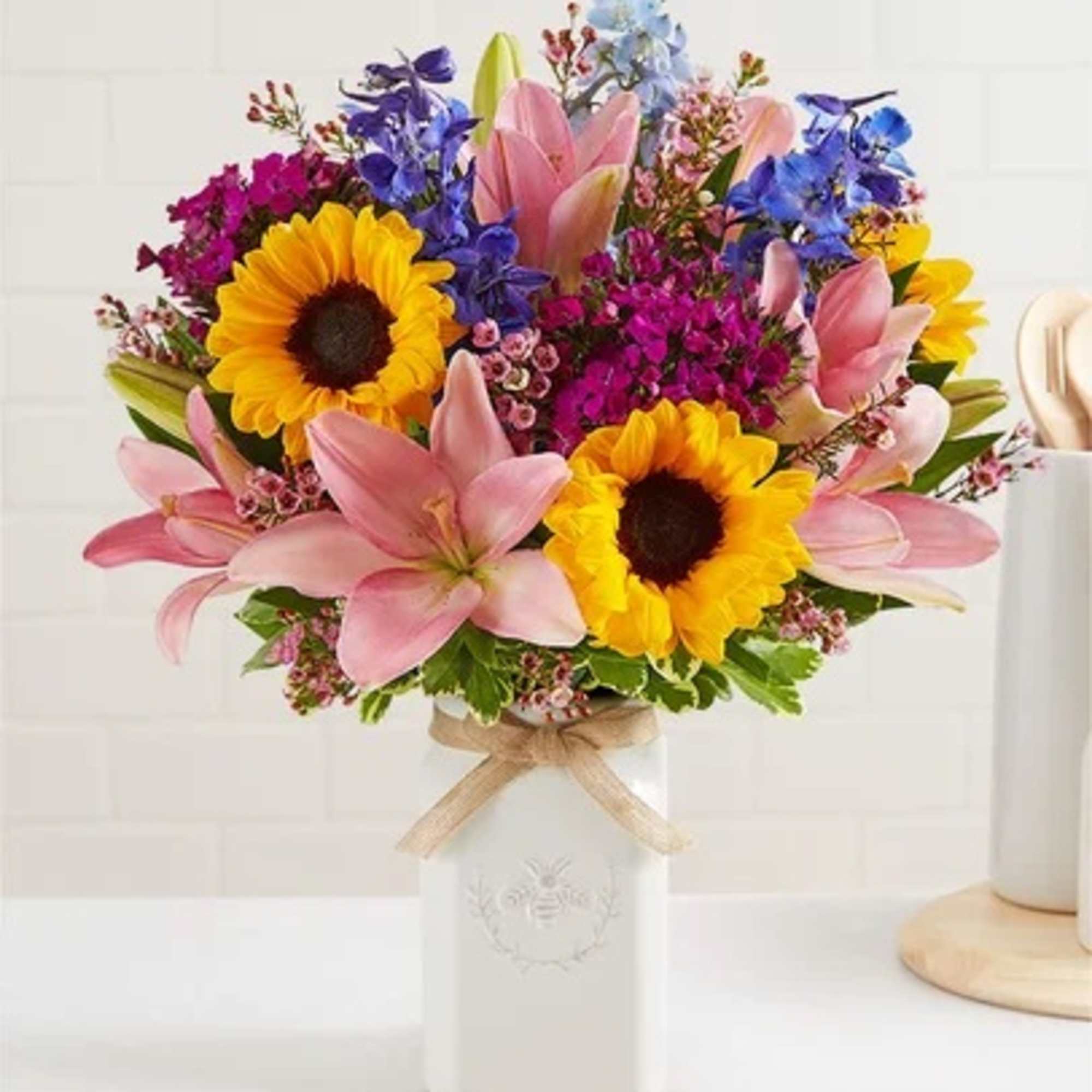 Bouquet of sunflowers, pink lilies, and blue flowers in a white vase