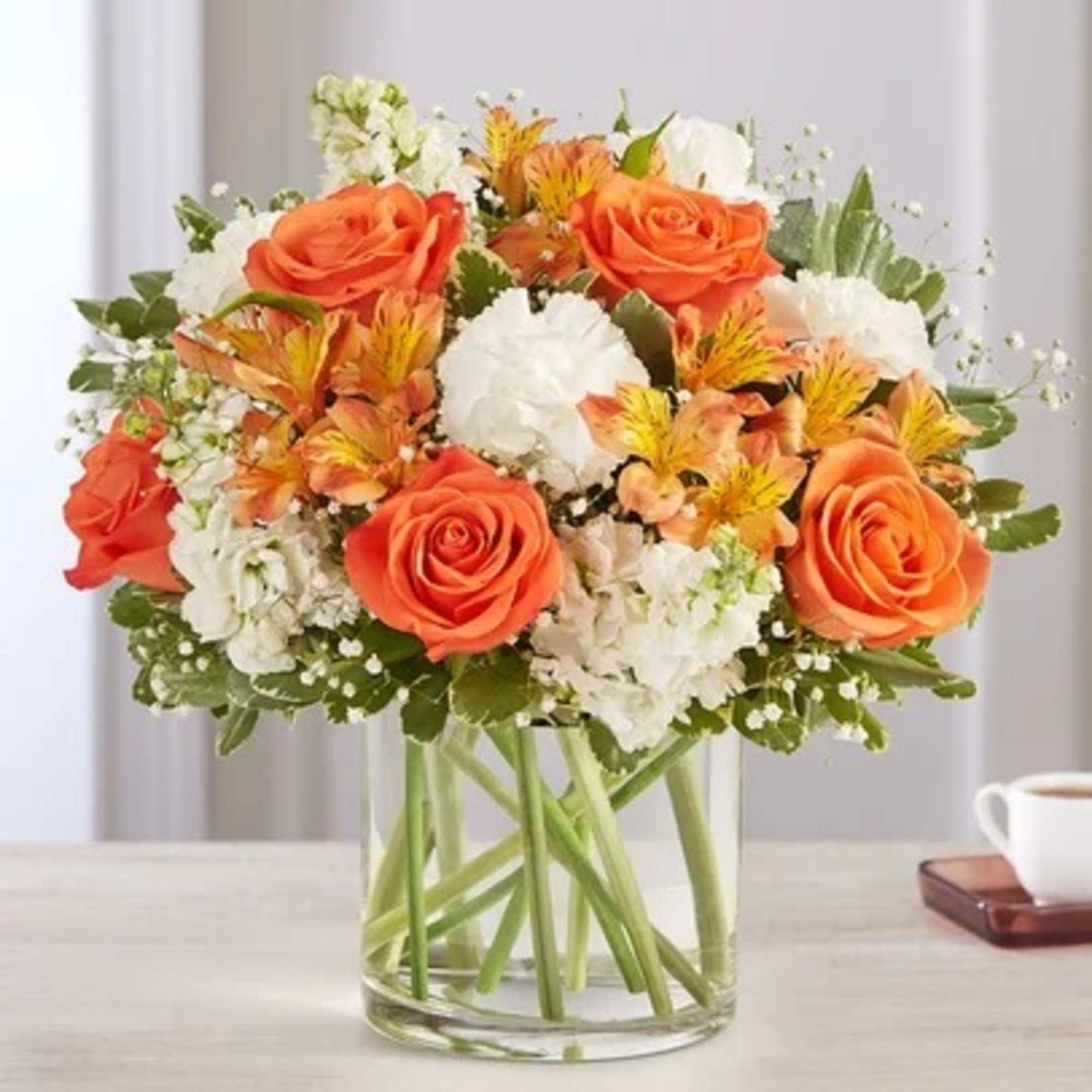 Orange roses and white flowers arranged in a clear glass vase