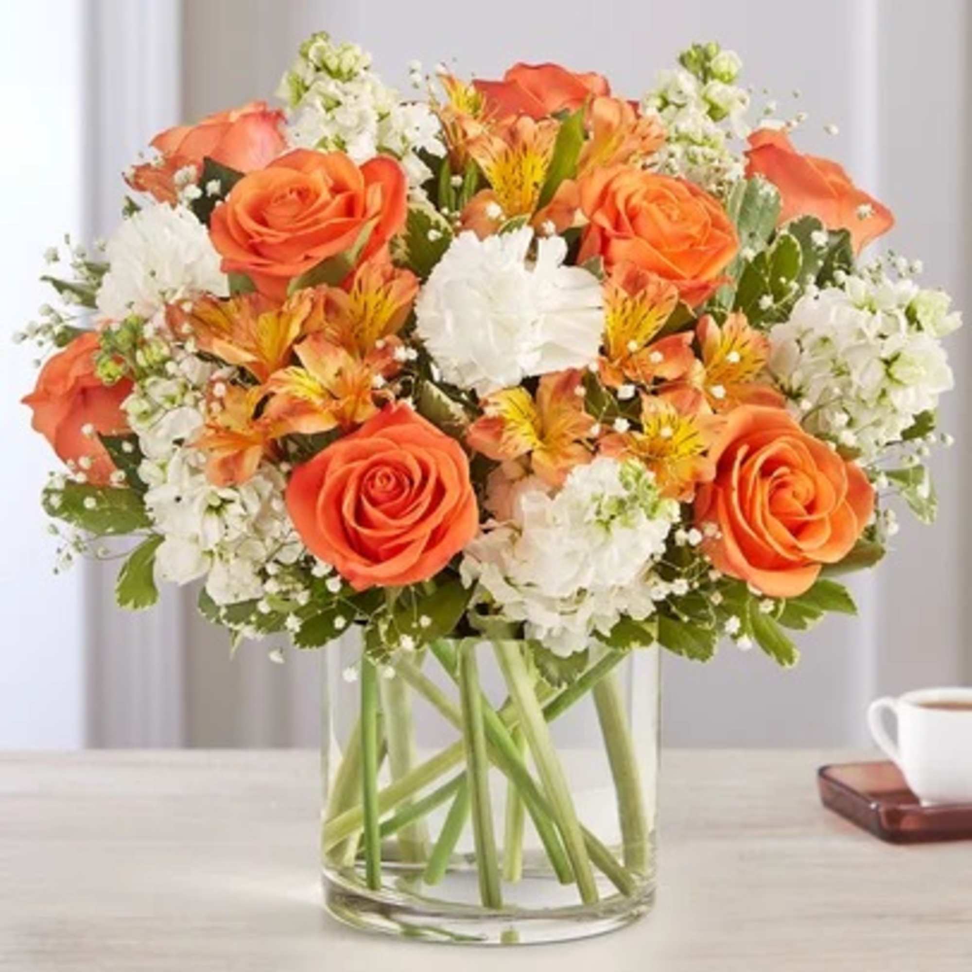 Orange roses and white flowers arranged in a clear glass vase