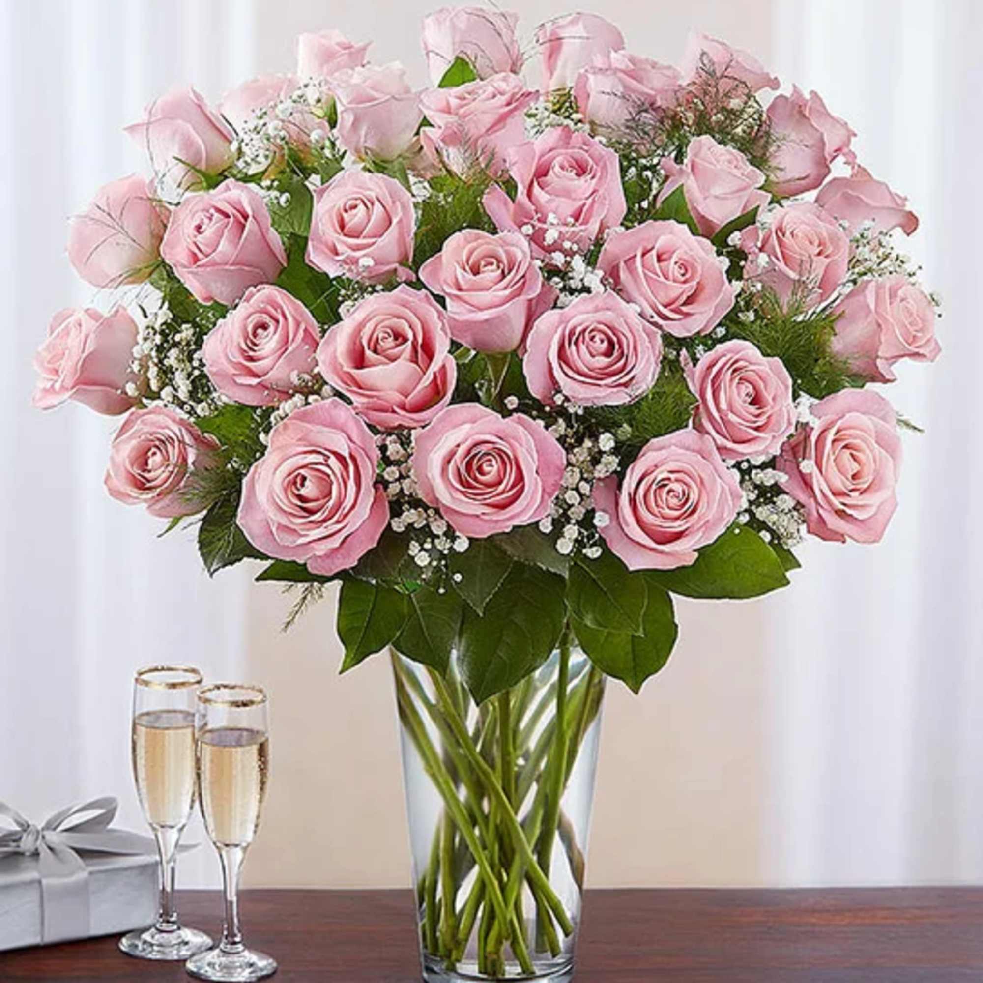 Pink roses arranged in a clear glass vase with two champagne flutes nearby