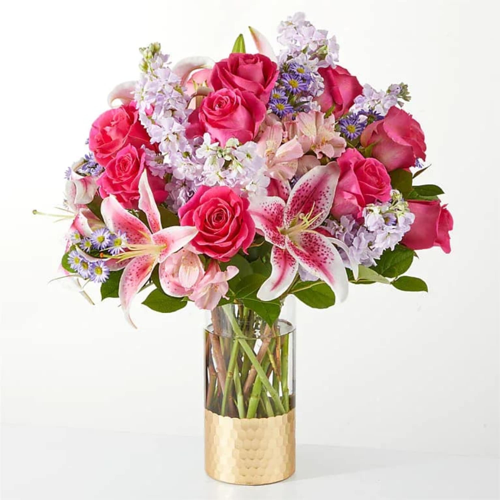 Pink roses and lilies arranged in a clear glass vase with a gold base