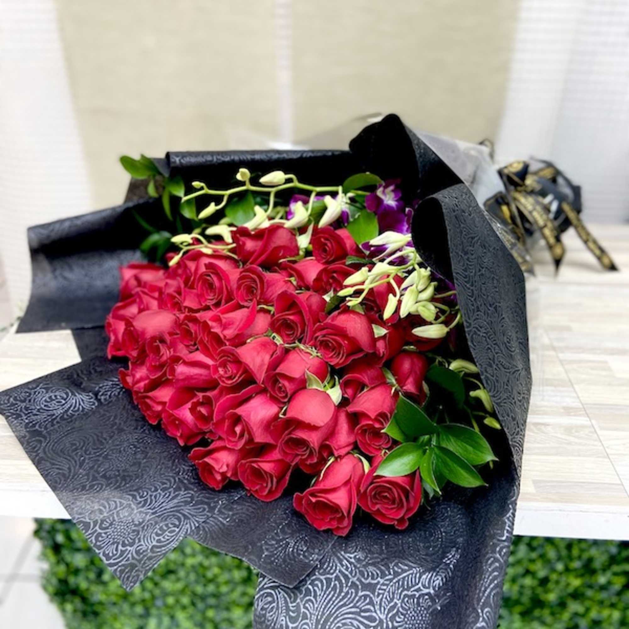 Large bouquet of red roses with accent orchids wrapped in black patterned paper