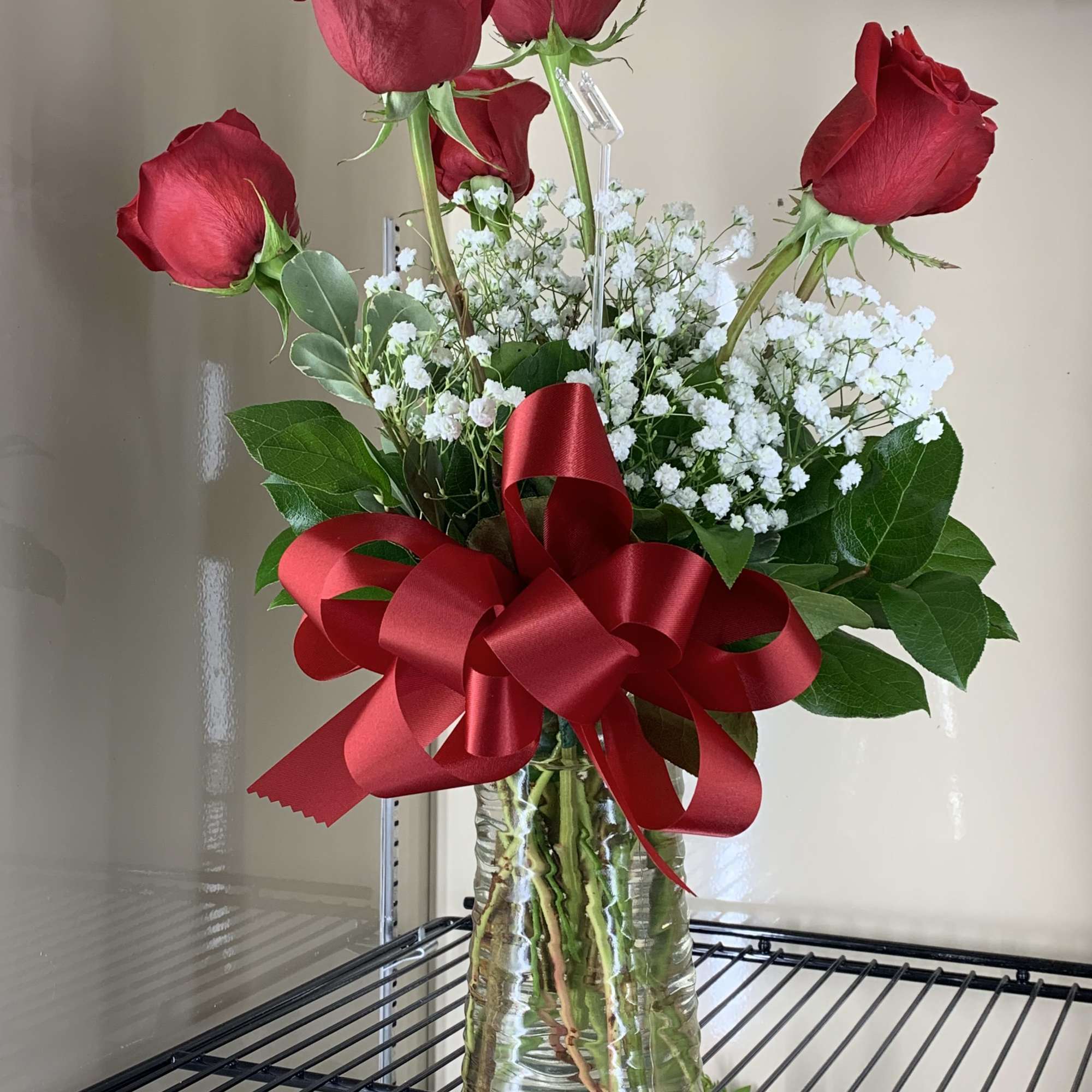 Red roses in a glass vase with baby's breath and a red ribbon