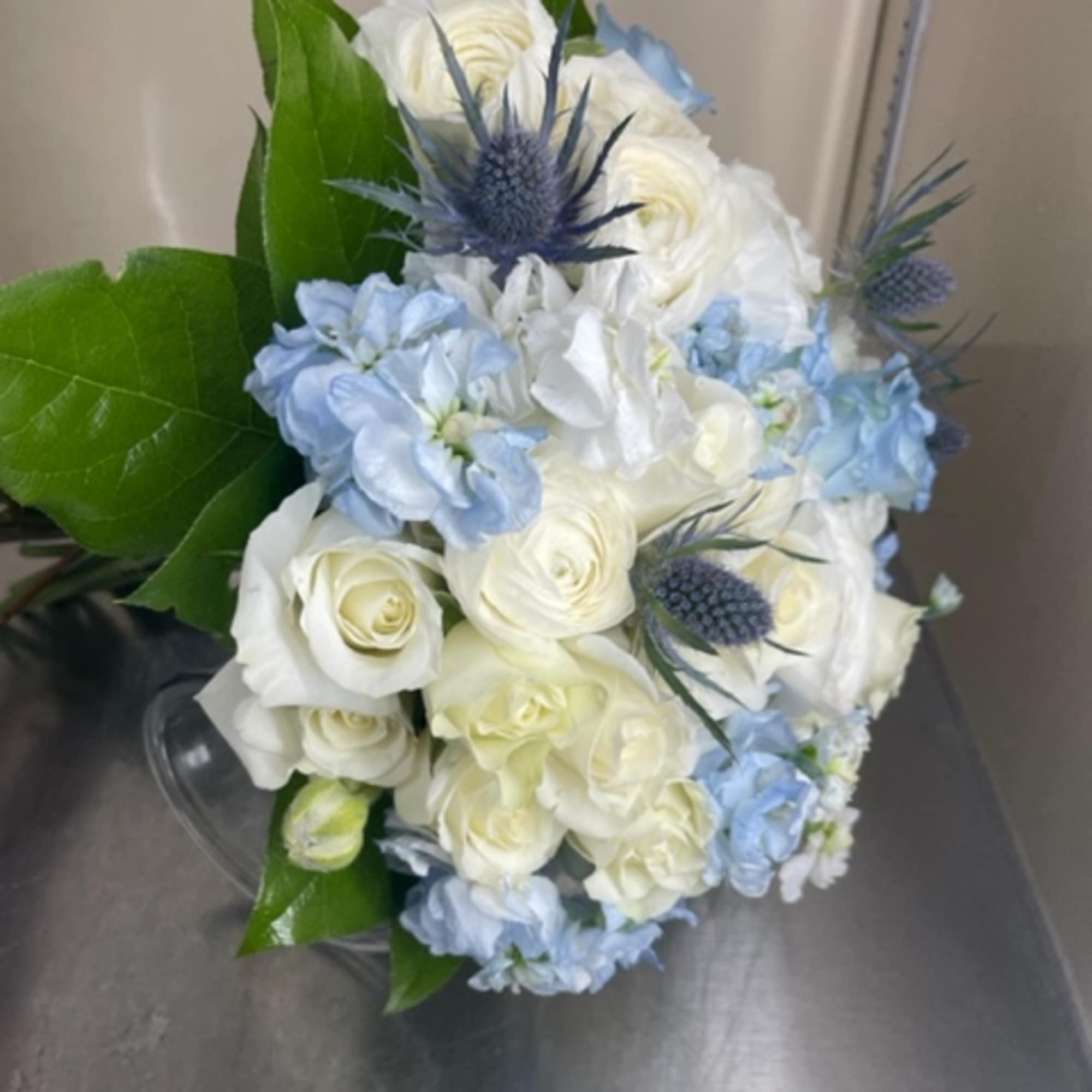 Bouquet of white roses and pale blue flowers with spiky blue thistles