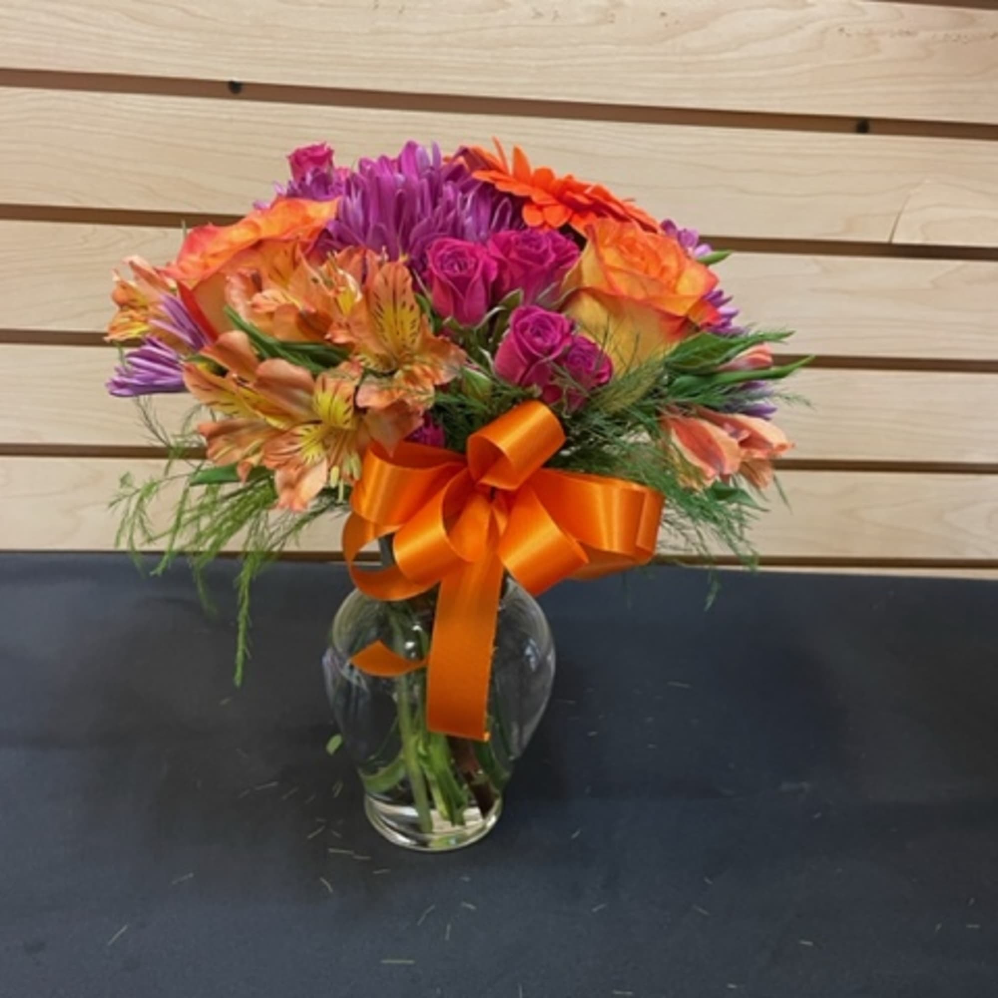 Colorful bouquet of mixed flowers in a glass vase with an orange ribbon