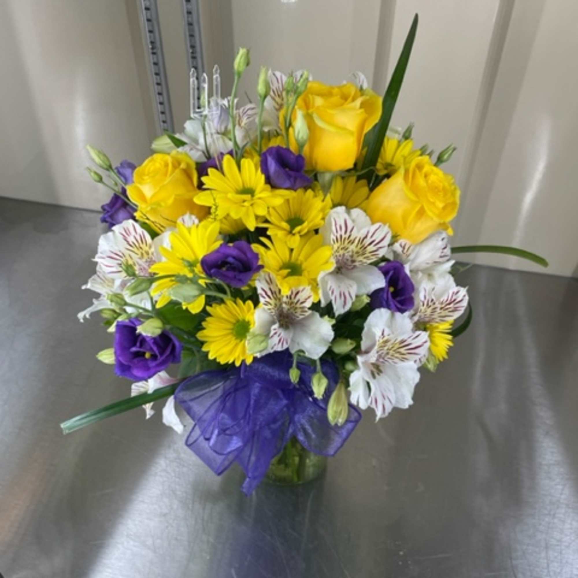 Bouquet of yellow roses, purple blooms, and white striped flowers in a glass vase
