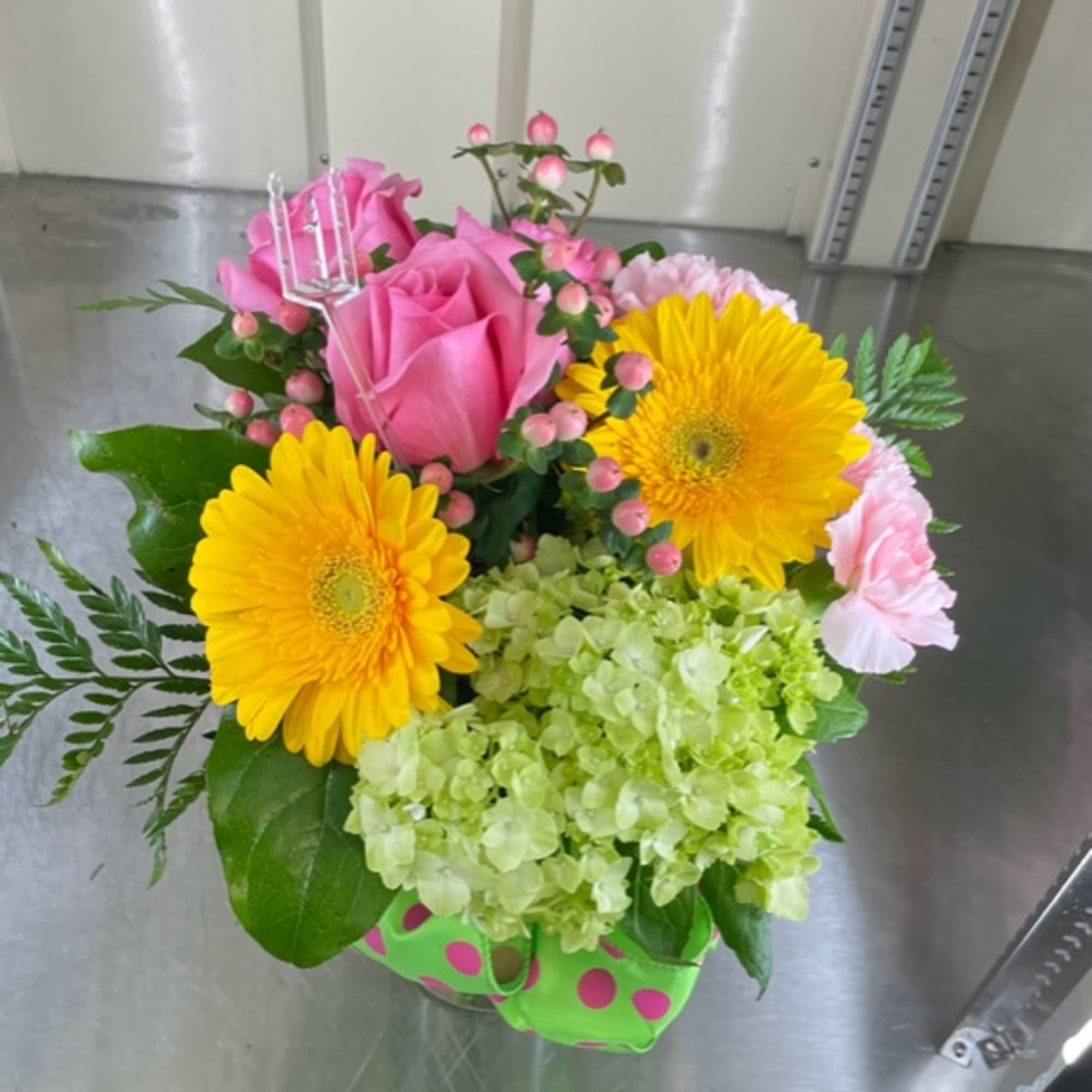 Pink roses and yellow gerbera daisies in a green polka-dot container