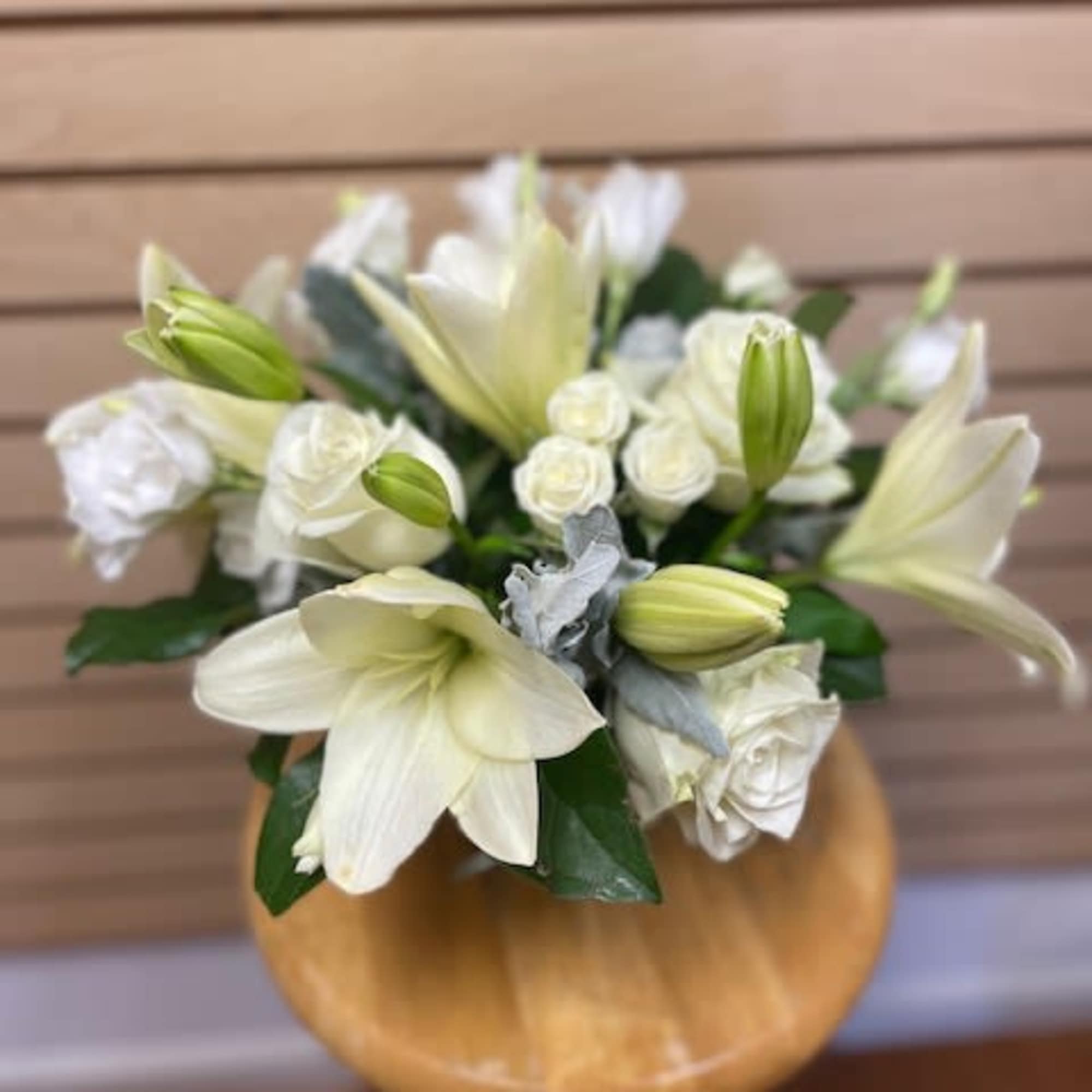 White lilies and roses arranged in a round wooden vase