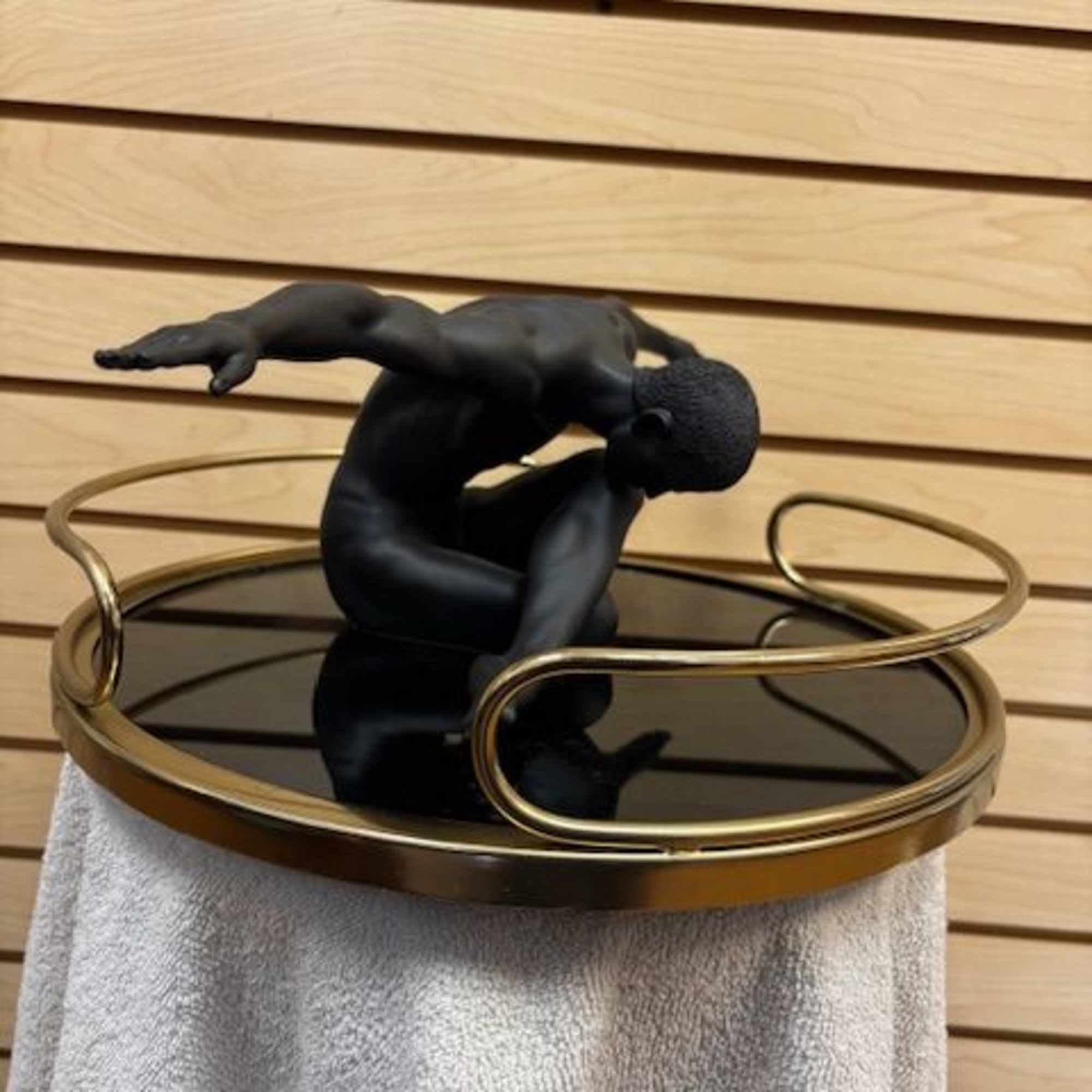 Black sculptural figure on a round gold tray over a textured pedestal