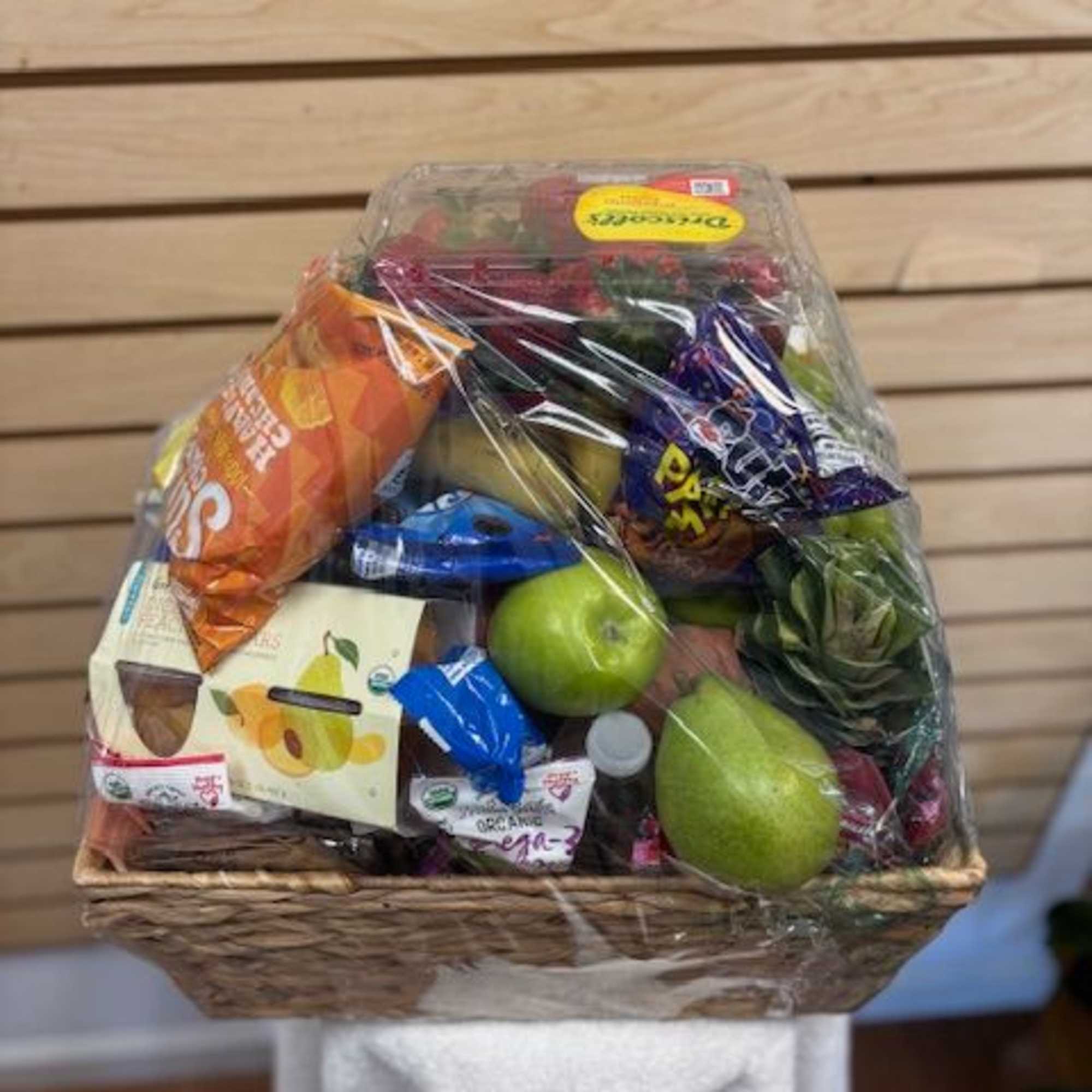 Gift basket with fruit and assorted packaged snacks wrapped in plastic