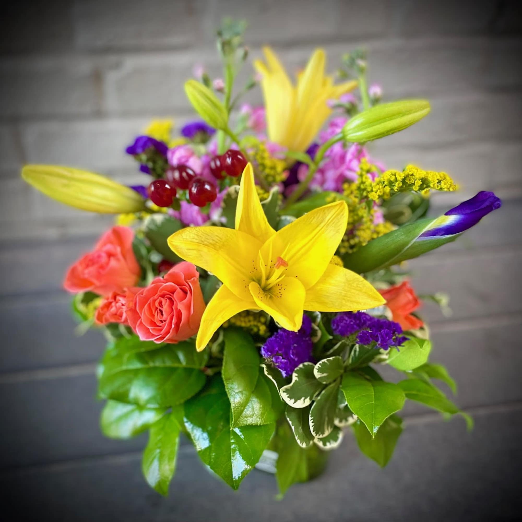 Bright mixed bouquet with yellow lilies, coral roses, and purple accents in a vase