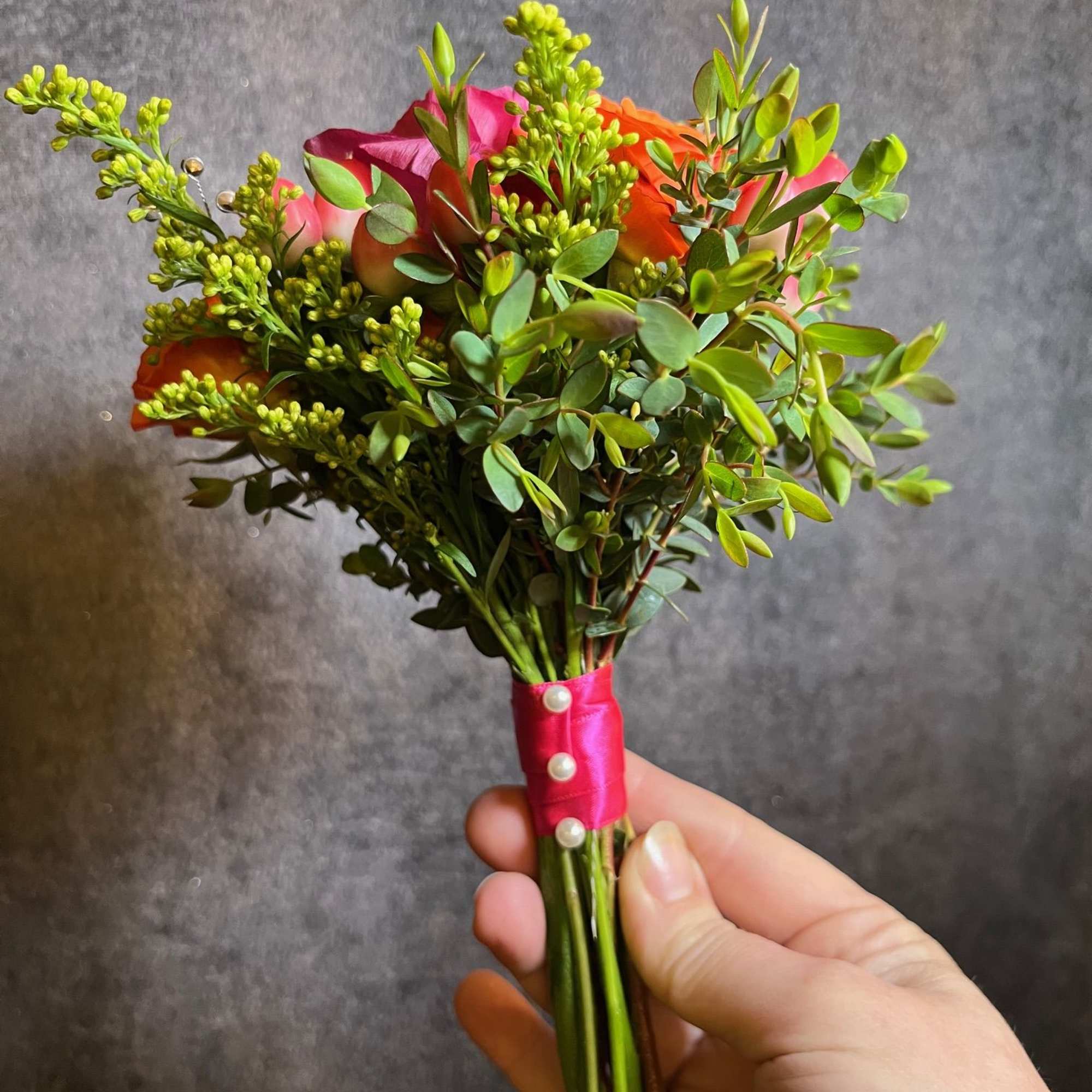 Small hand-tied bouquet of pink and orange roses with greenery