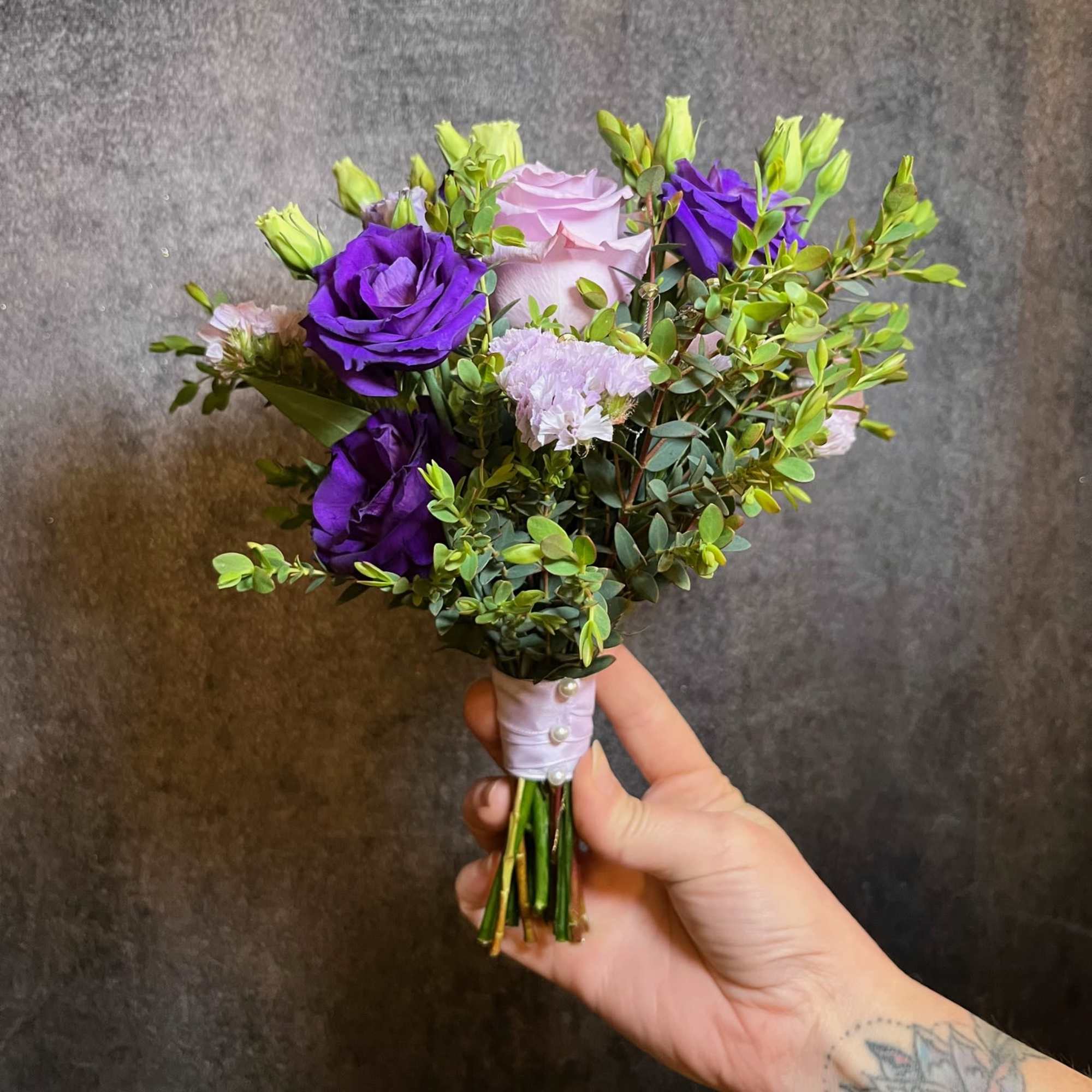 Handheld bouquet of purple and pale pink flowers with greenery