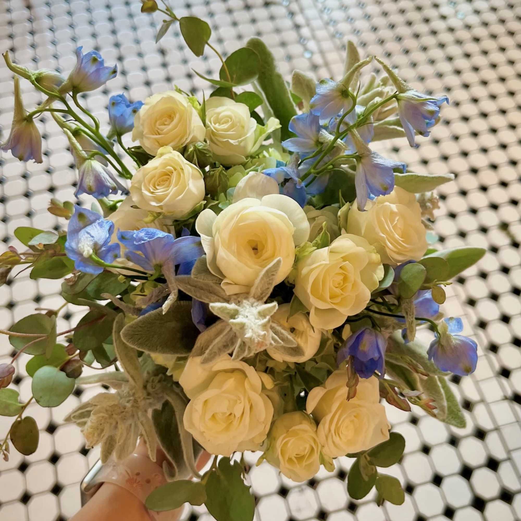 Handheld bouquet of cream roses and blue flowers