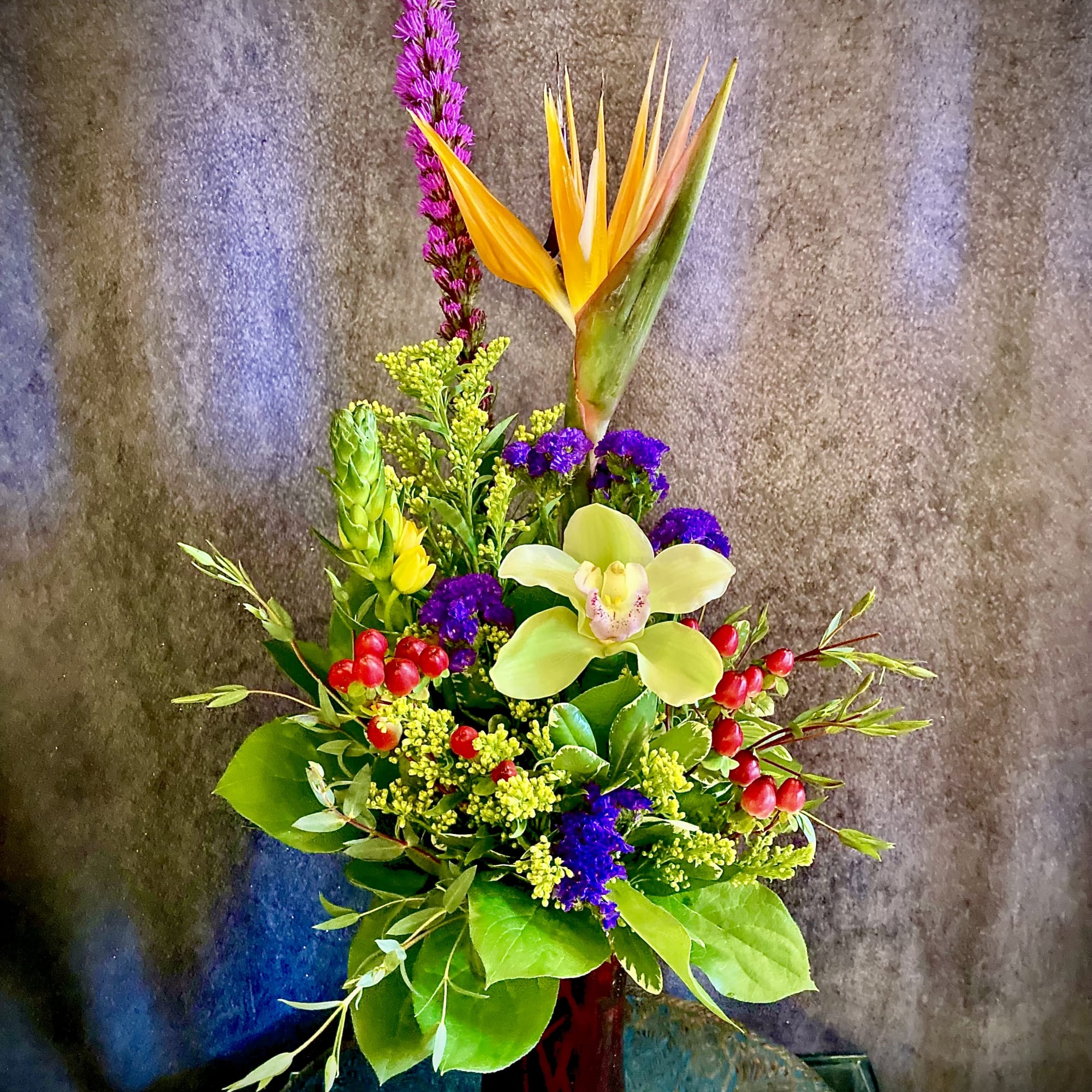 A dramatic vertical silhouette anchored by a bird-of-paradise and pale green cymbidium
