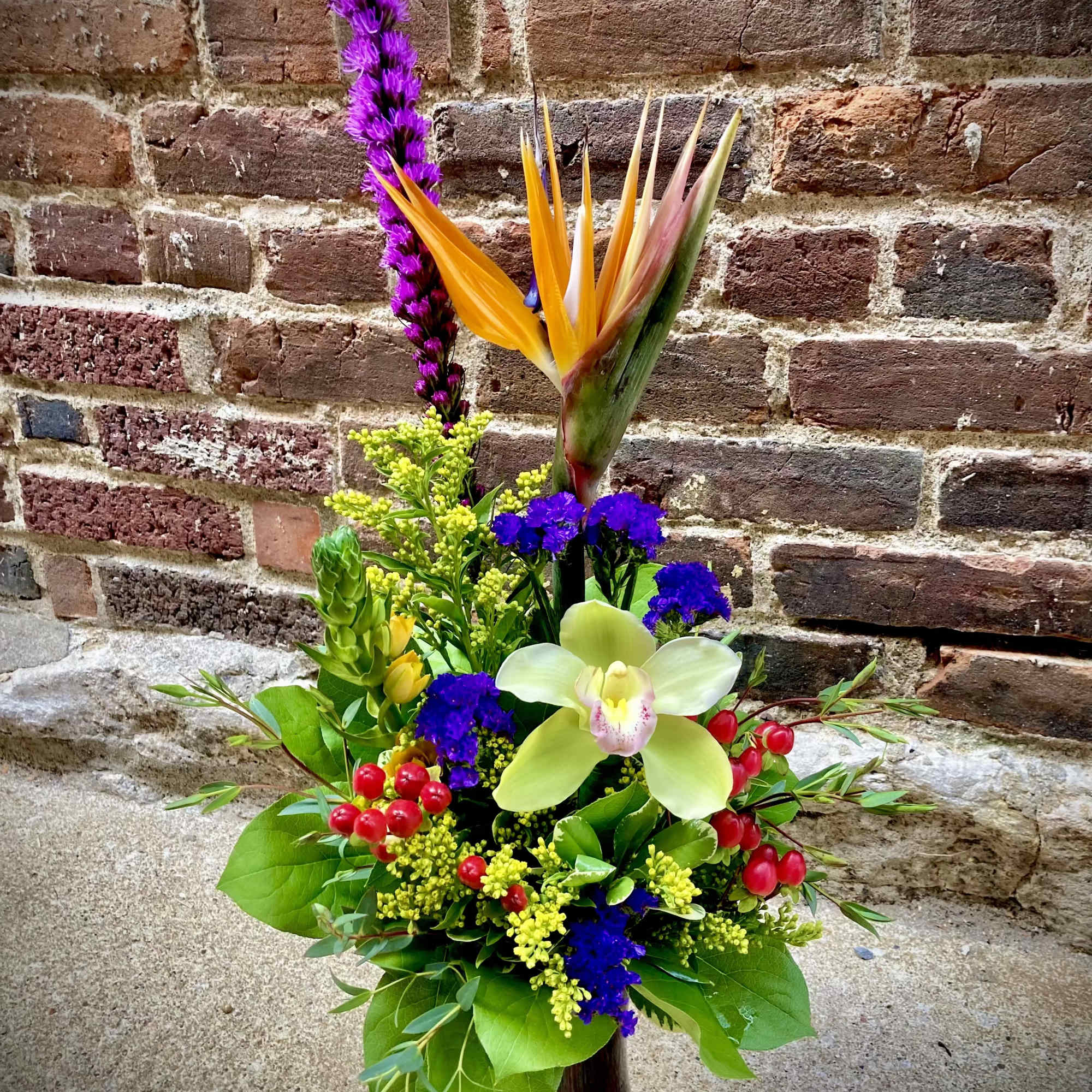 A dramatic vertical silhouette anchored by a bird-of-paradise and pale green cymbidium