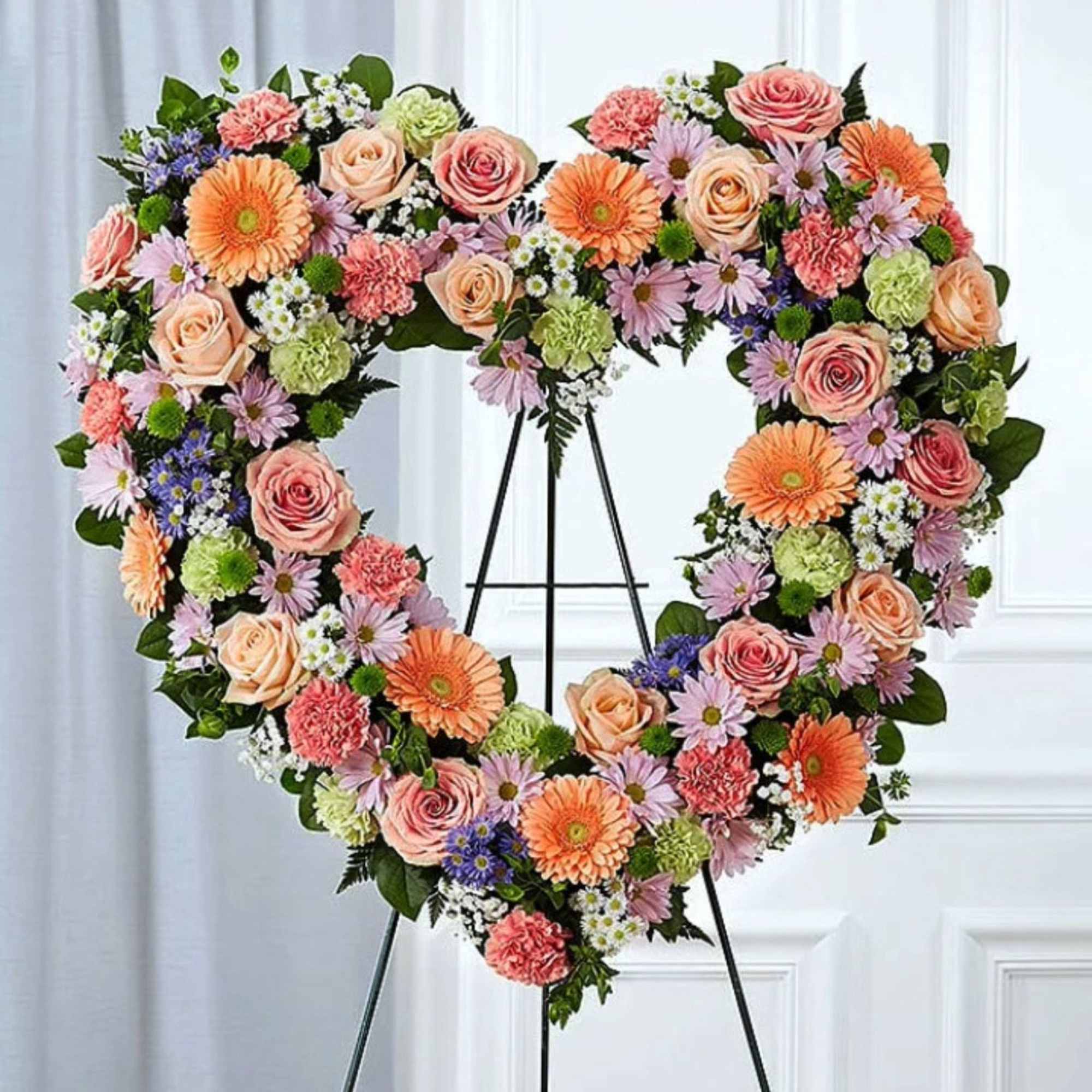 Heart-shaped floral wreath on a stand with roses, daisies, and gerbera daisies