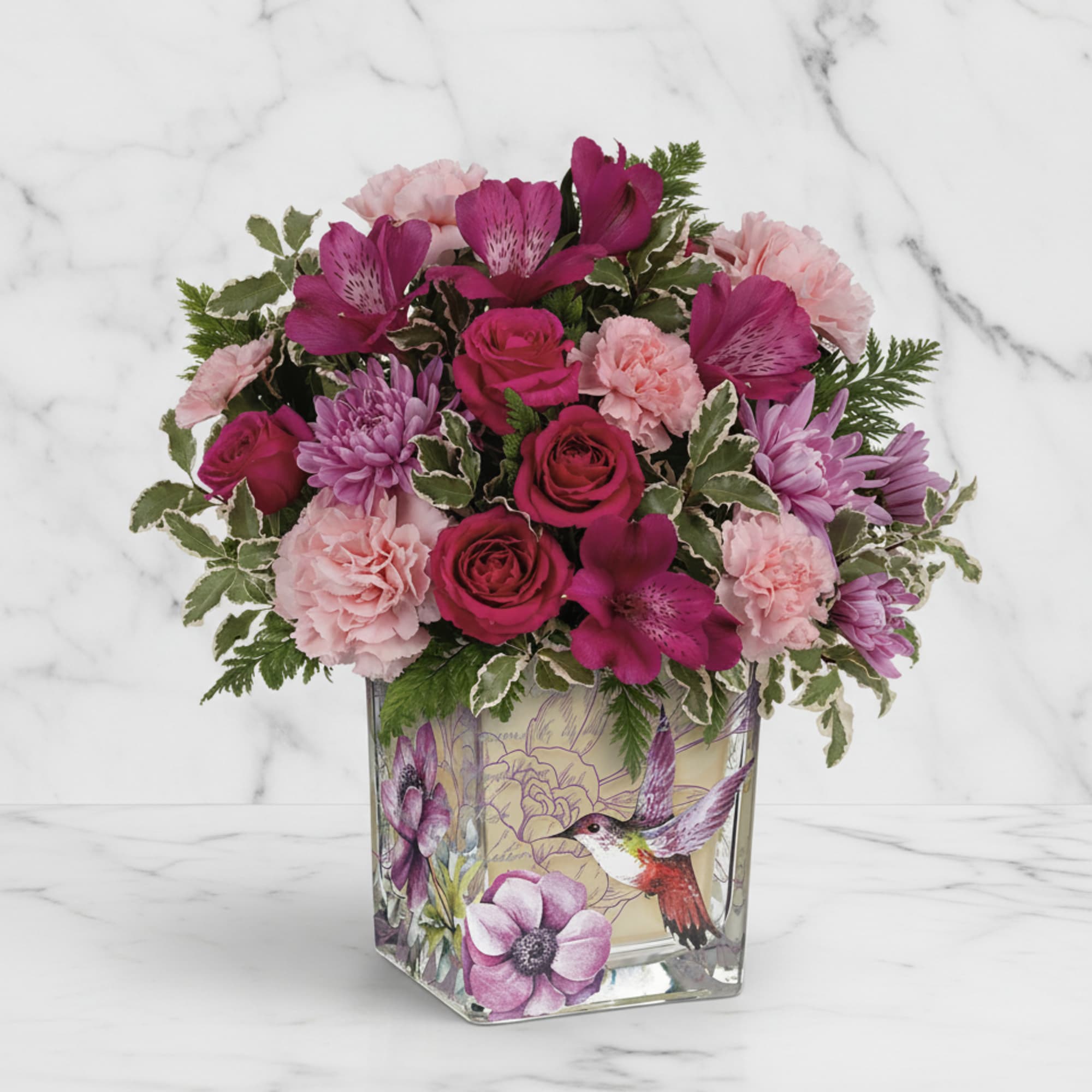 Pink and magenta flowers arranged in a square glass vase with a bird design