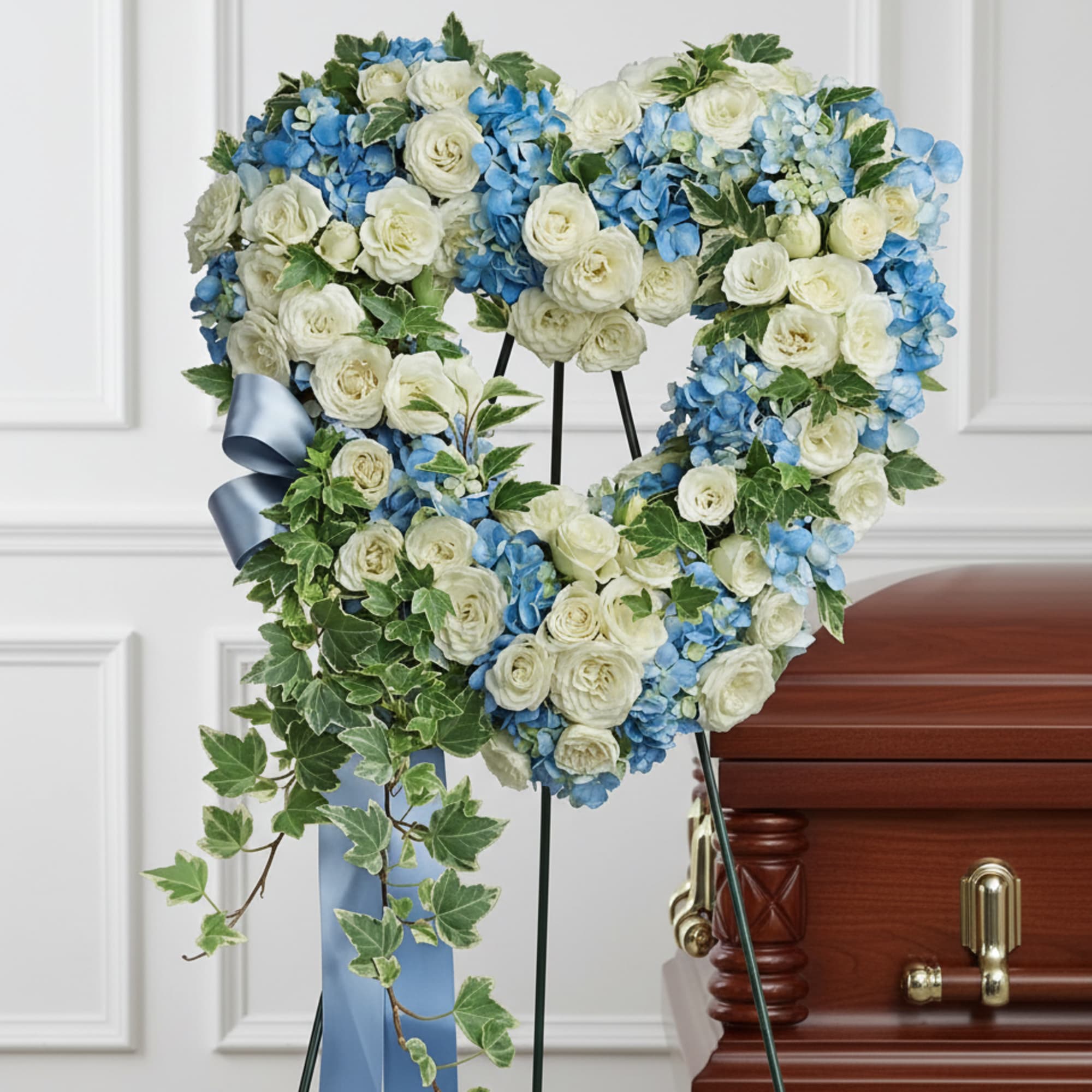 Heart-shaped floral wreath with white roses and blue hydrangeas on a stand