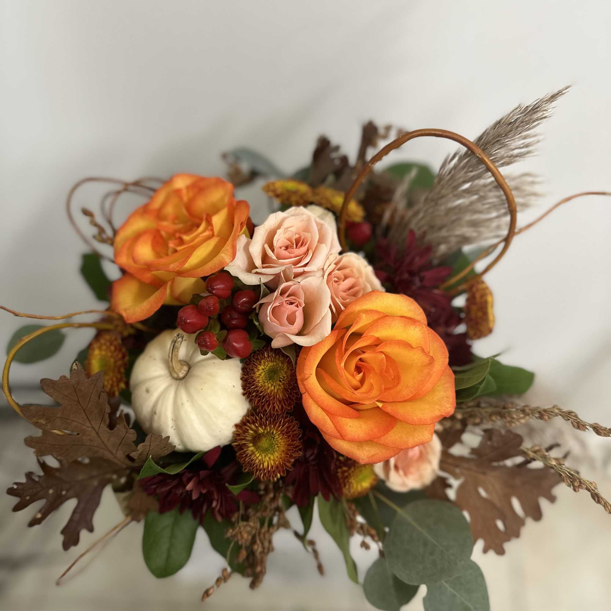Autumn arrangement with orange and peach roses, burgundy mums, berries and a white mini pumpkin