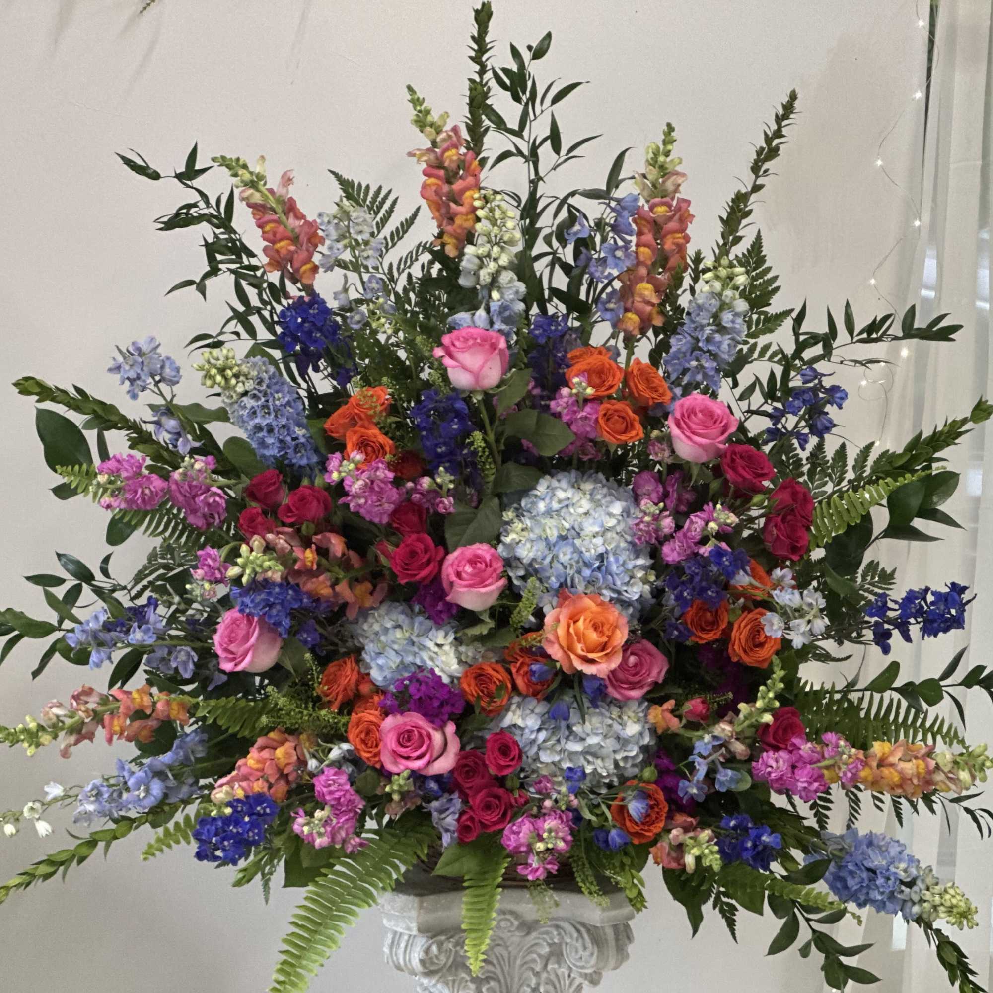 Large colorful floral arrangement in a white pedestal vase
