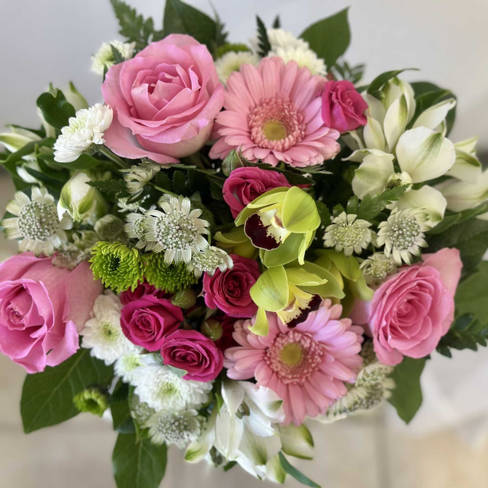 Pink roses and gerbera daisies with white filler flowers and green orchids