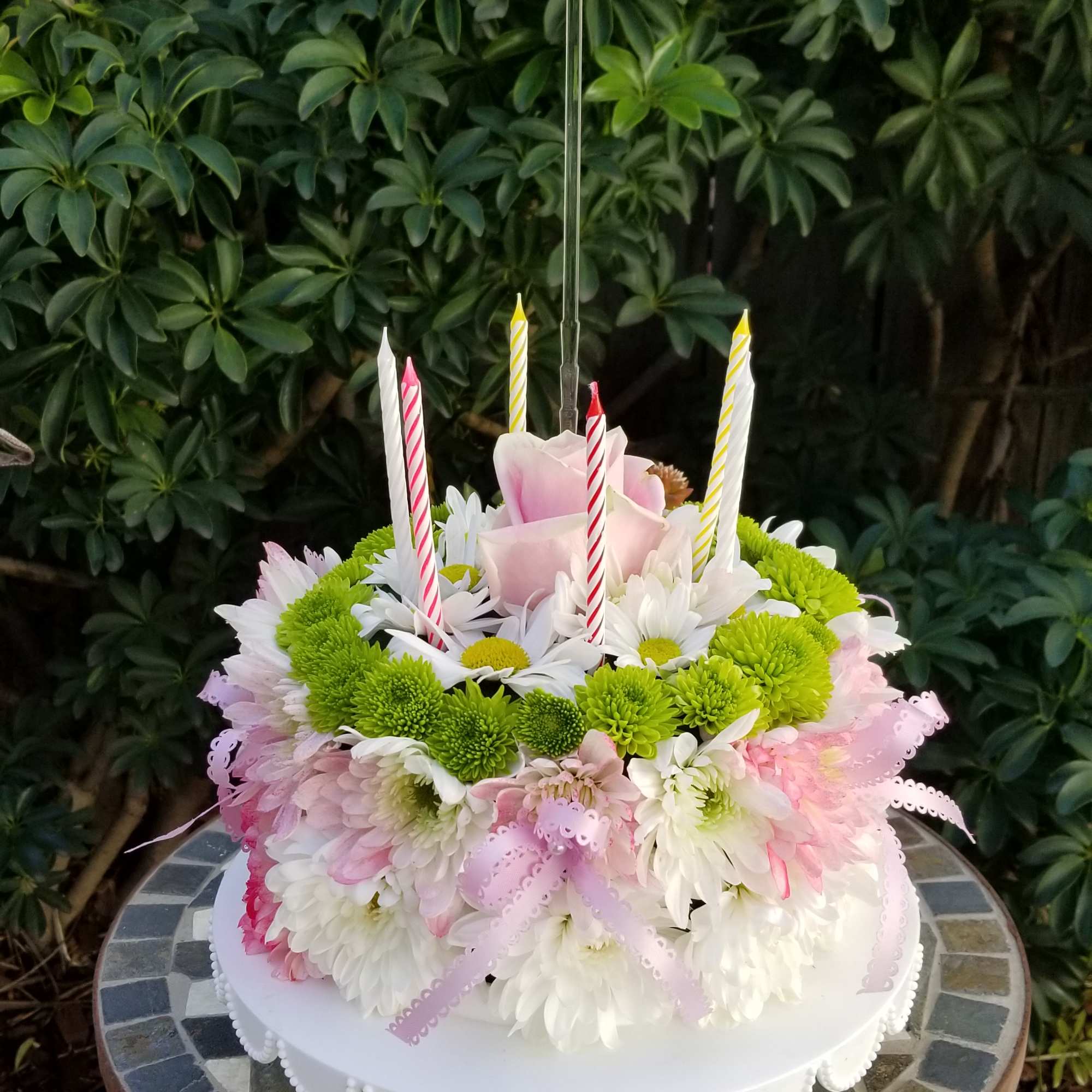 Round floral cake with candles and a pink rose topper