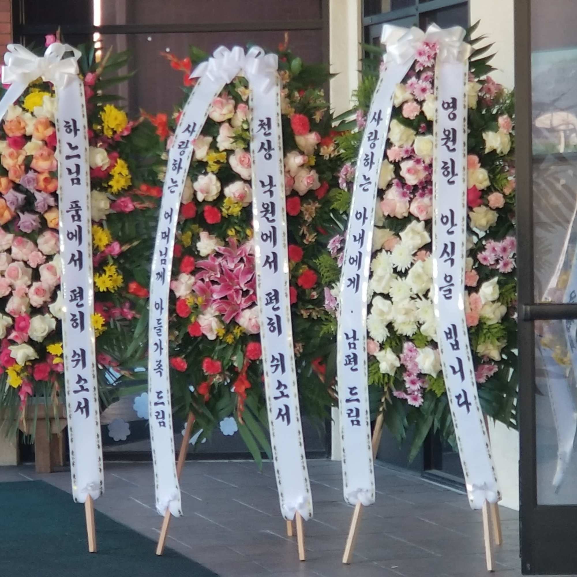 Tall standing funeral wreaths with white ribbons and mixed flowers