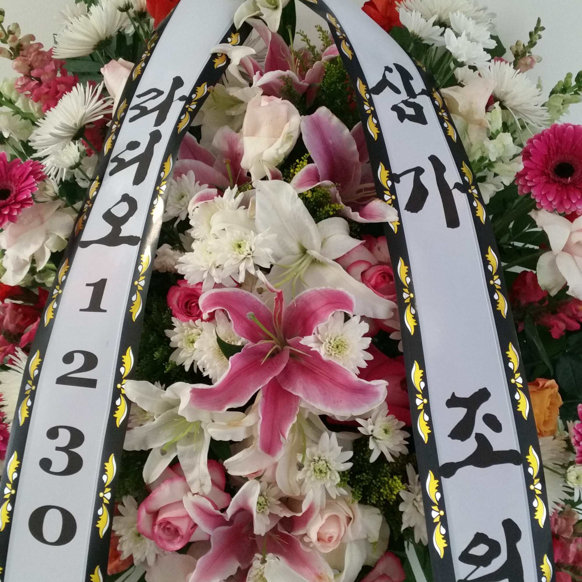 Standing floral wreath with lilies, roses, and white ribbon banners