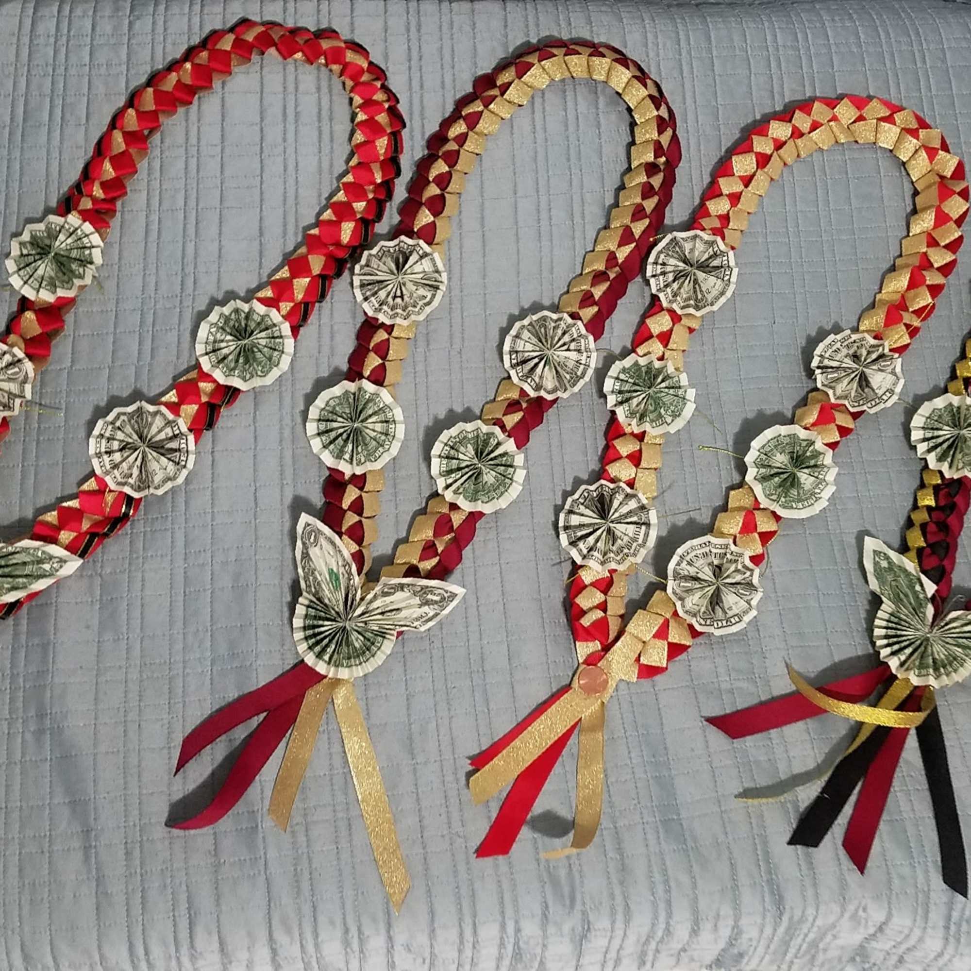 Four braided money garlands with ribbon tassels laid on a bed