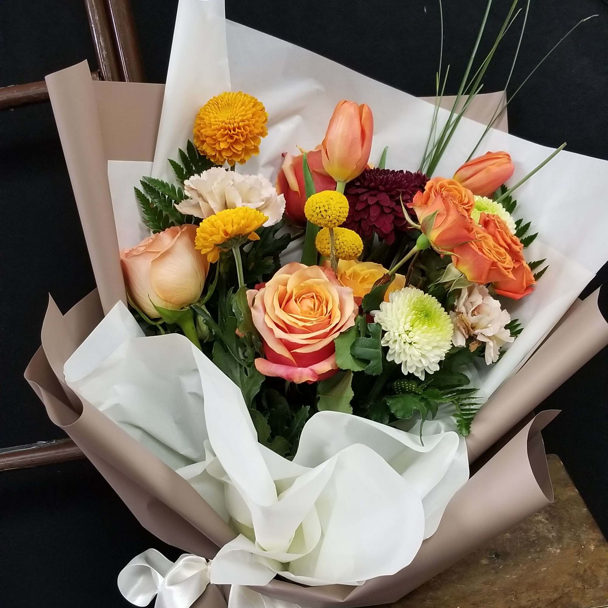 Bouquet of peach and orange roses with mixed chrysanthemums wrapped in beige and white paper