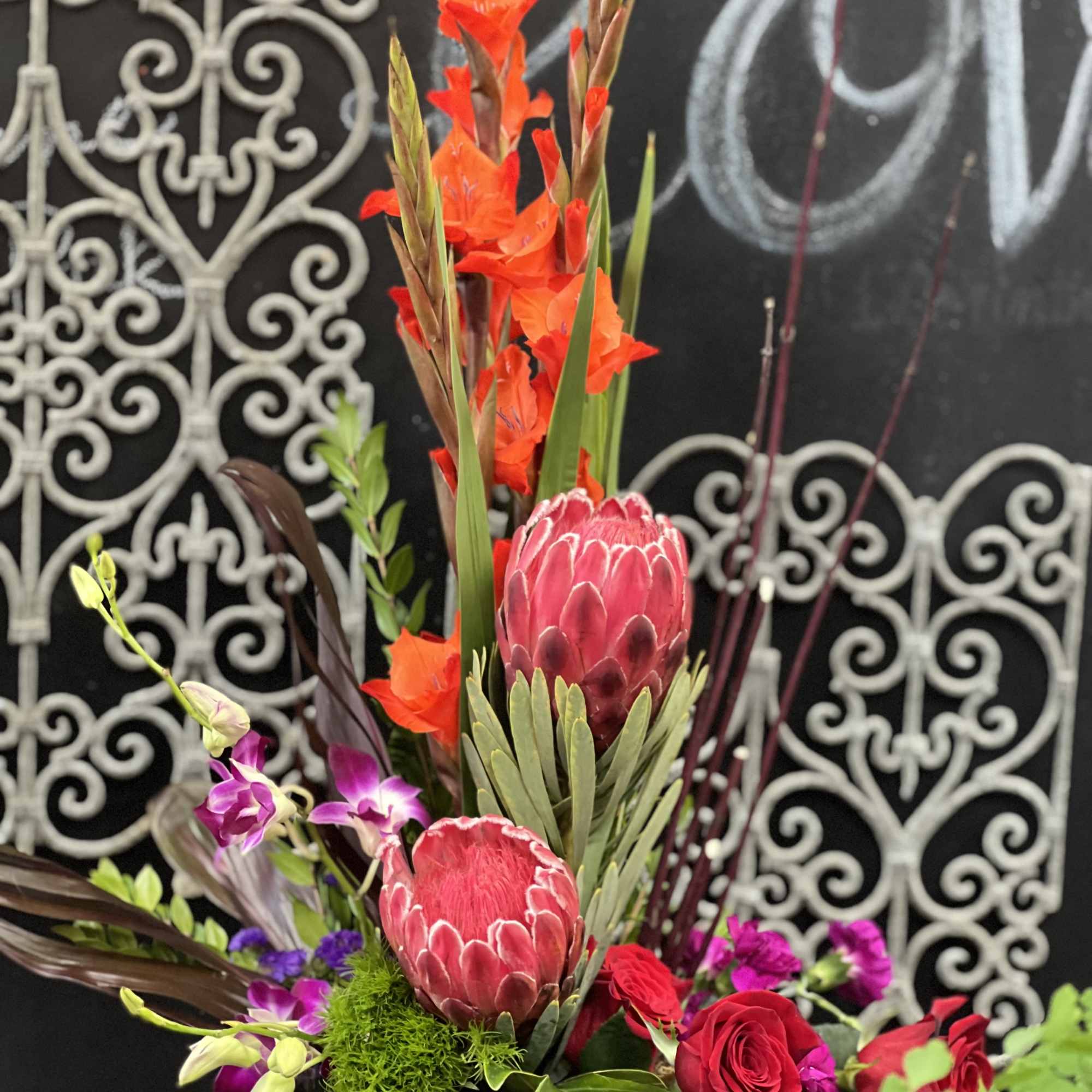 Tall tropical floral arrangement with red protea and orange blooms