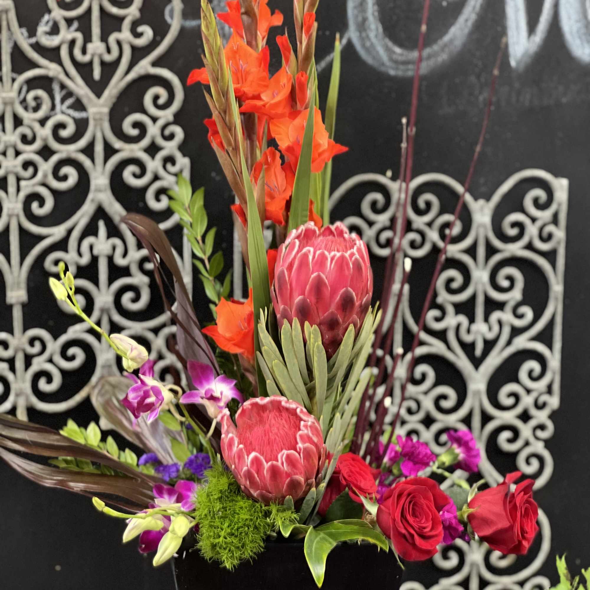 Tall floral arrangement with red roses and pink protea in a black vase