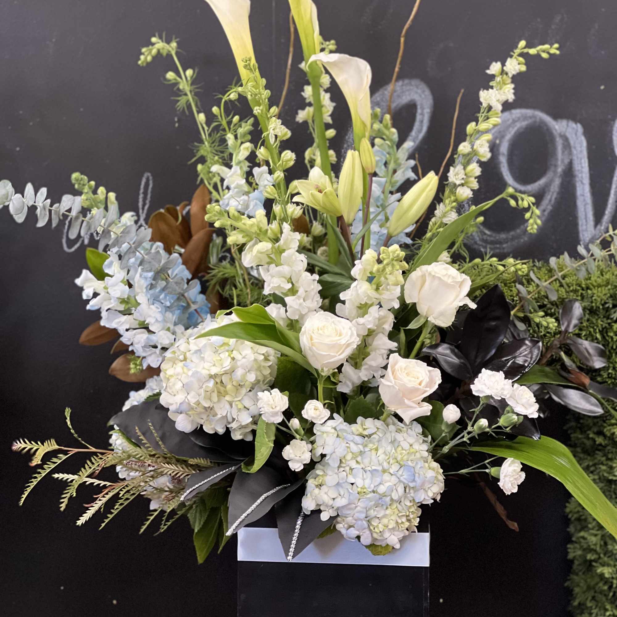 Tall white floral arrangement with lilies, roses, and hydrangeas in a black box