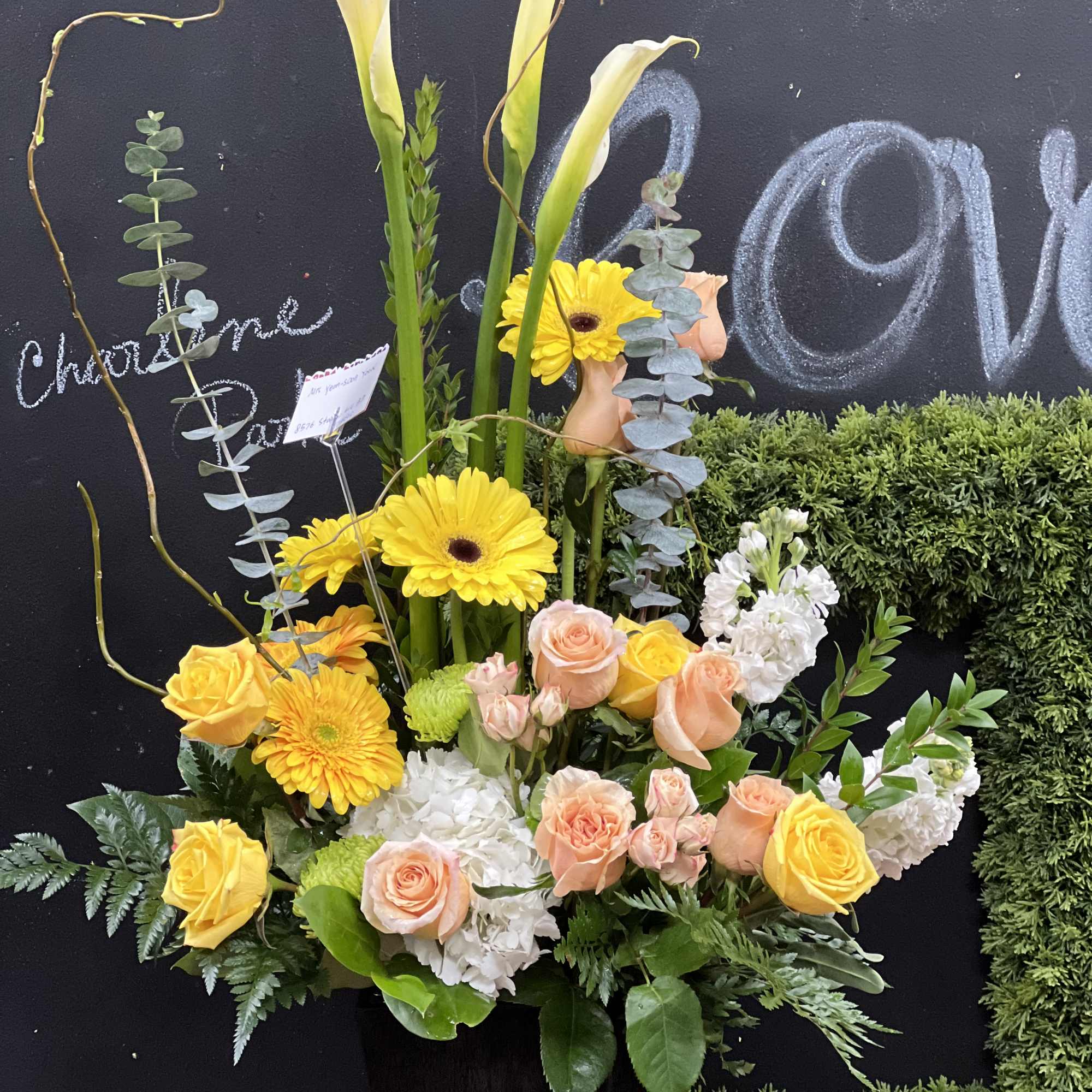 Tall floral arrangement with yellow calla lilies, roses, and gerbera daisies