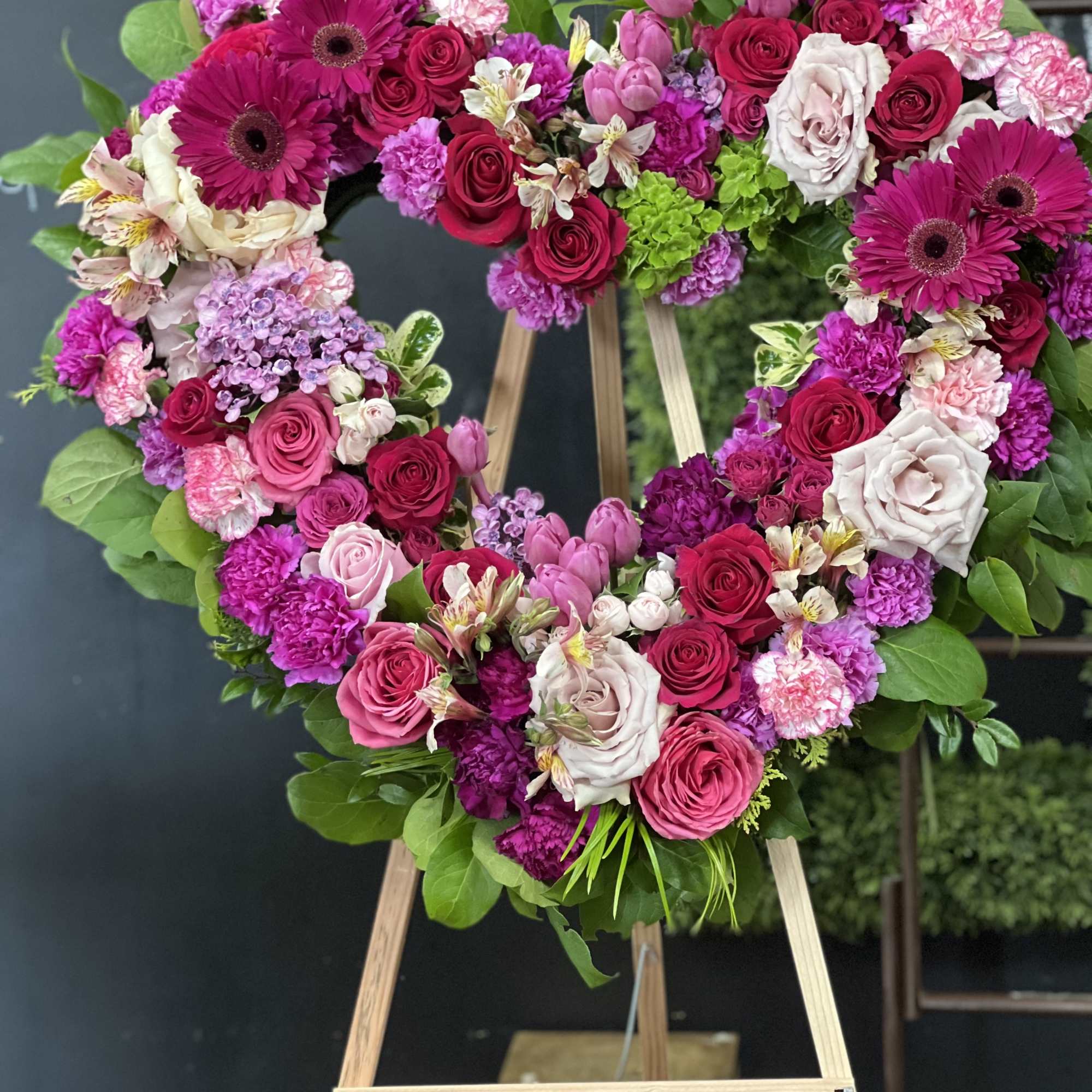 Heart-shaped floral wreath with pink and red roses on an easel