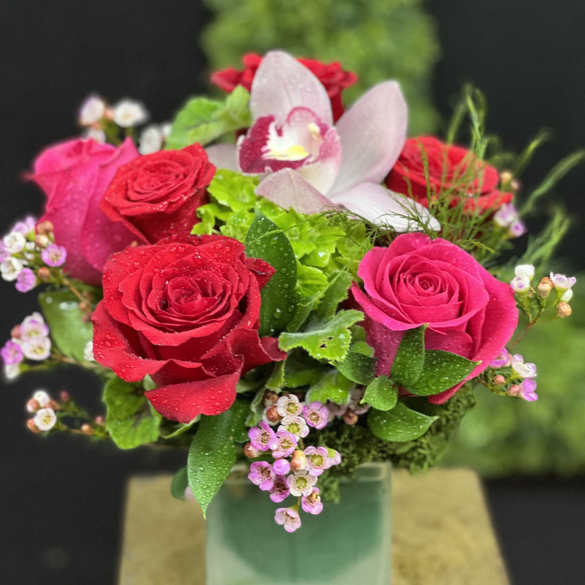 Pink and red roses with an orchid in a square glass vase