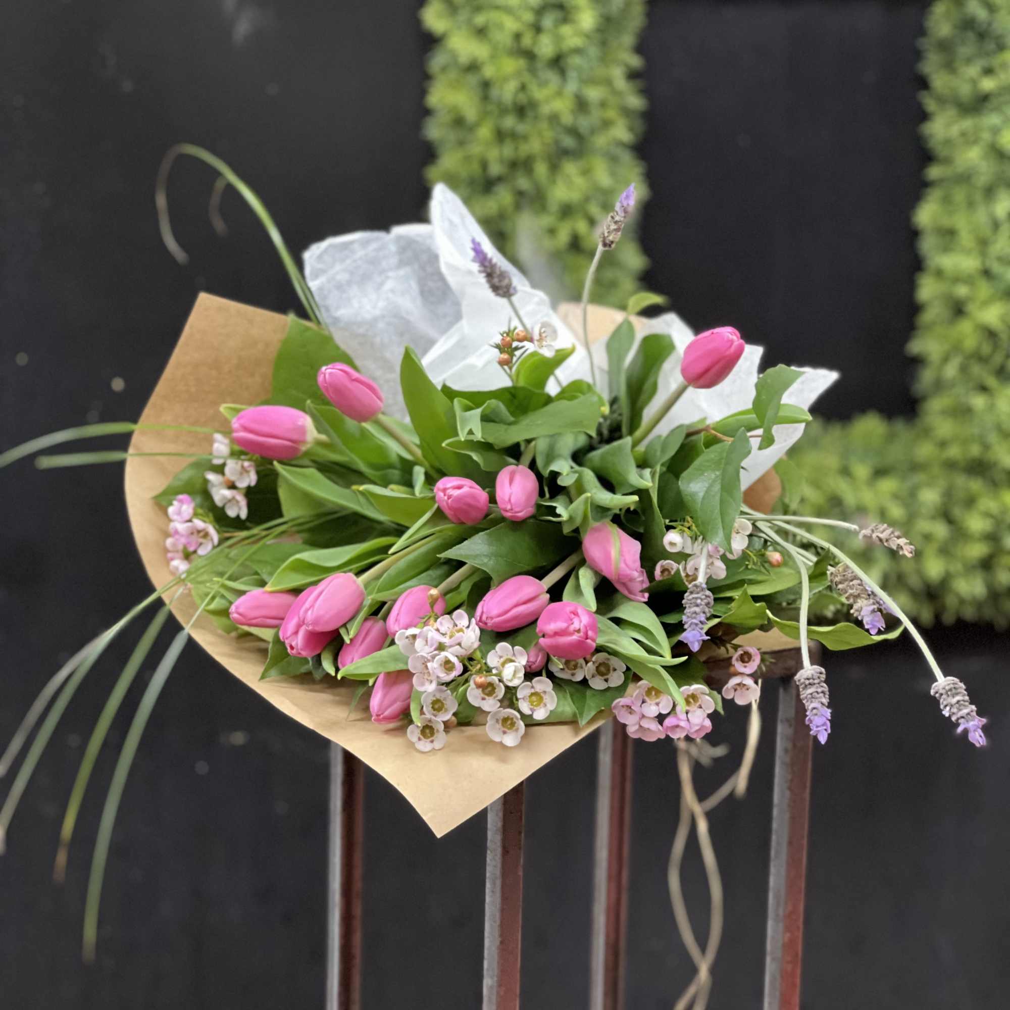Pink tulip bouquet with small white and lavender flowers wrapped in kraft paper