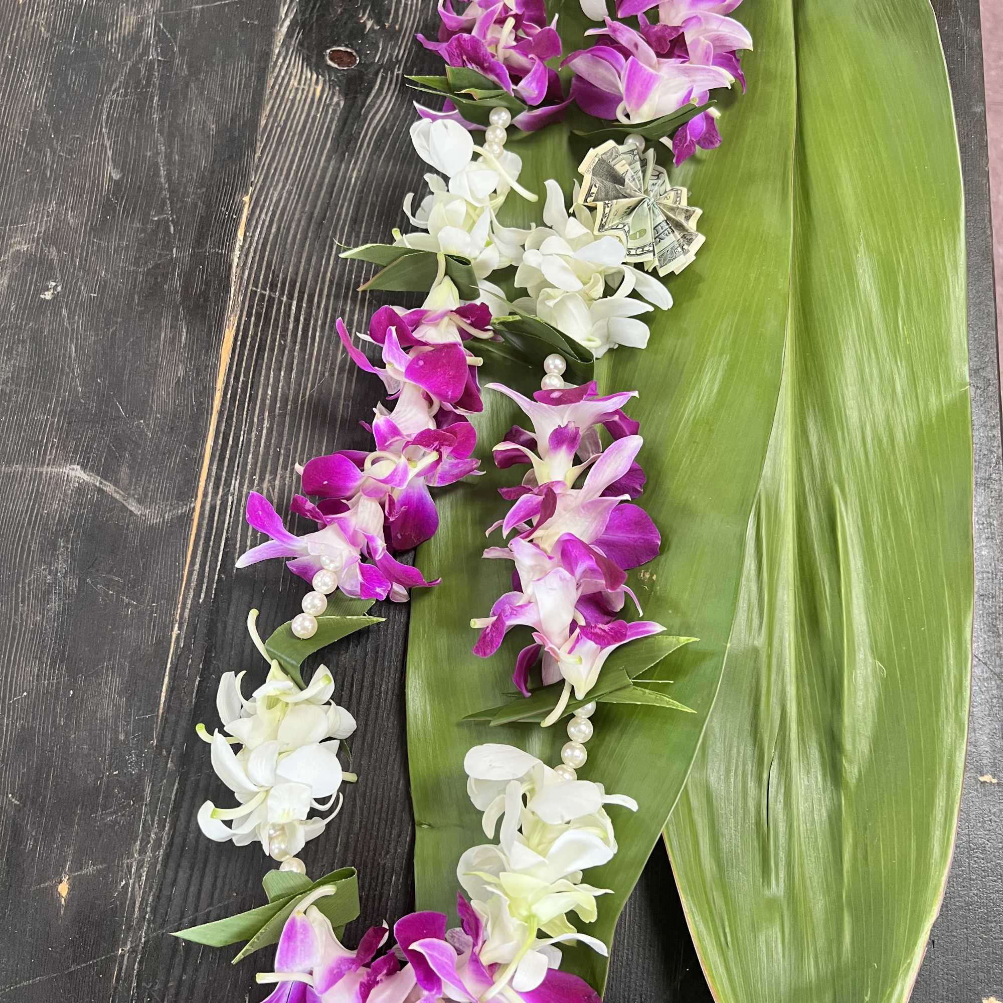 Purple and white orchid lei on large green leaves