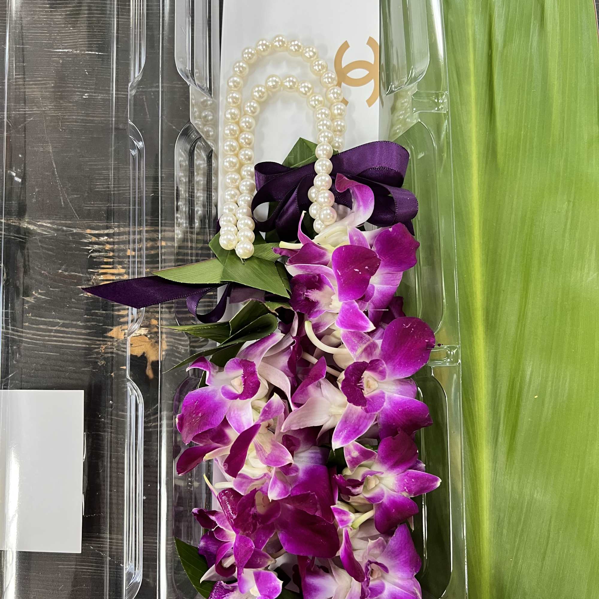 Purple orchid lei with pearl beads and ribbon in clear packaging