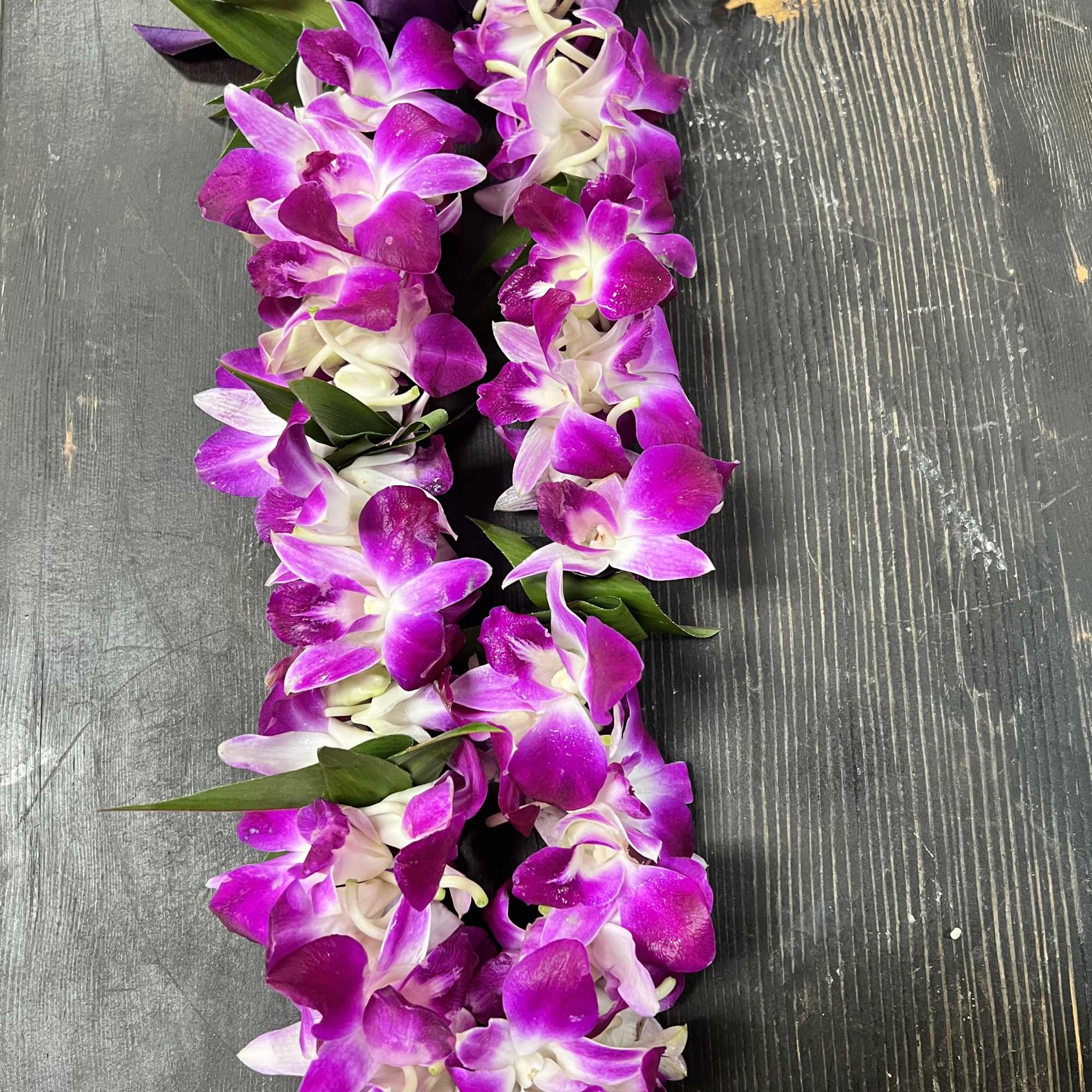 Purple orchid lei with pearl strands on a dark wood surface