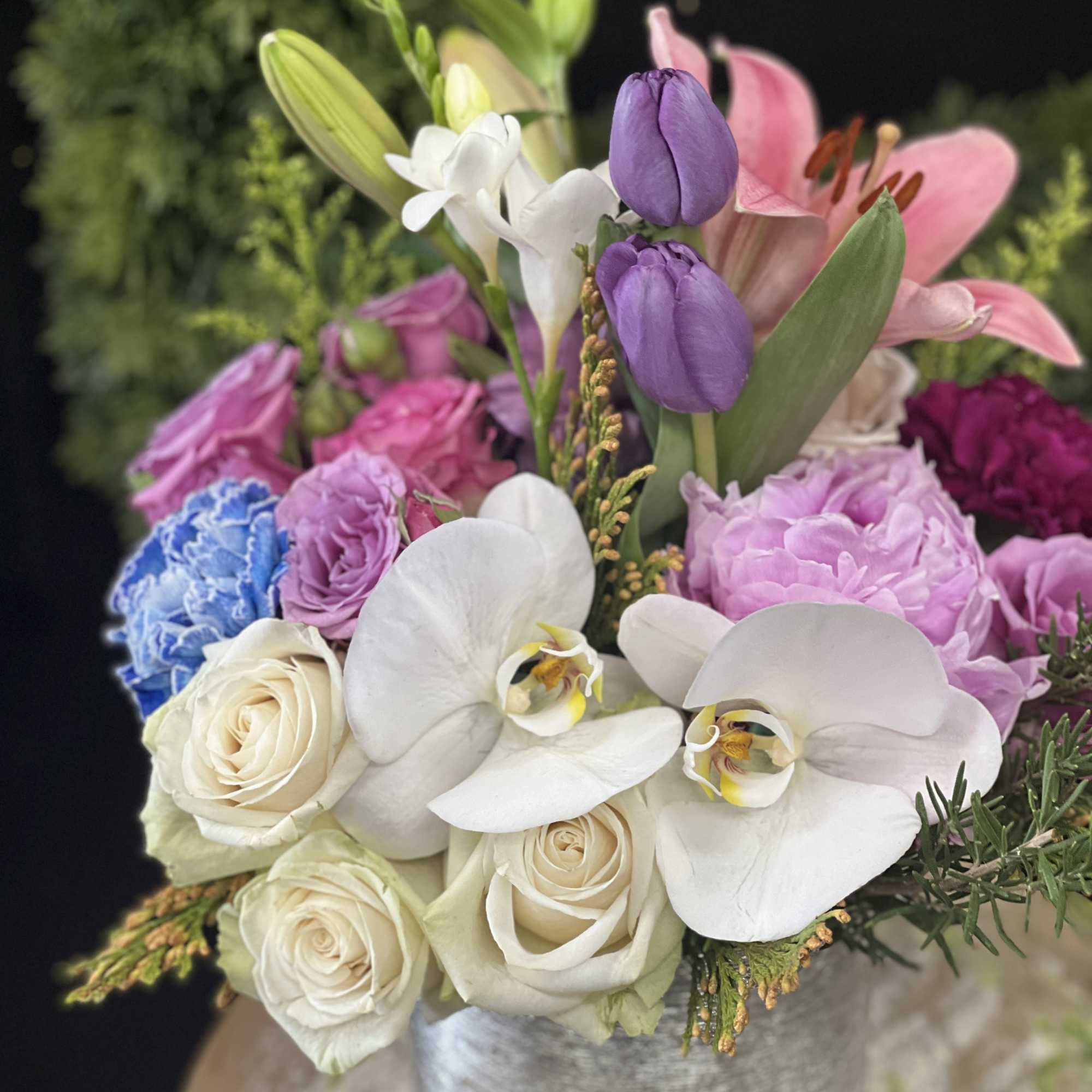 Mixed bouquet with white orchids, roses, lilies, and pink-purple blooms in a silver vase