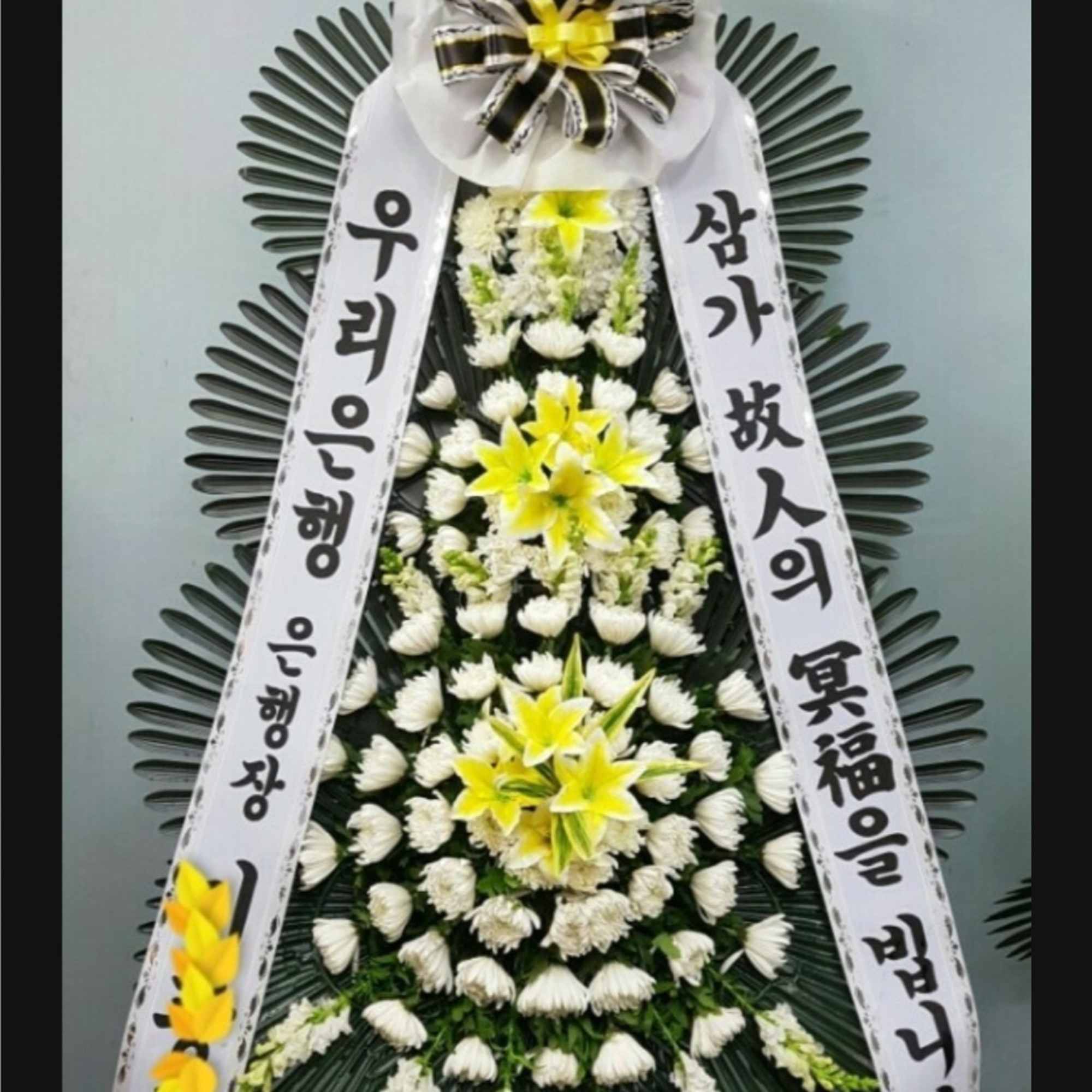 Tall funeral wreath with white flowers, yellow lilies, and Korean condolence ribbons