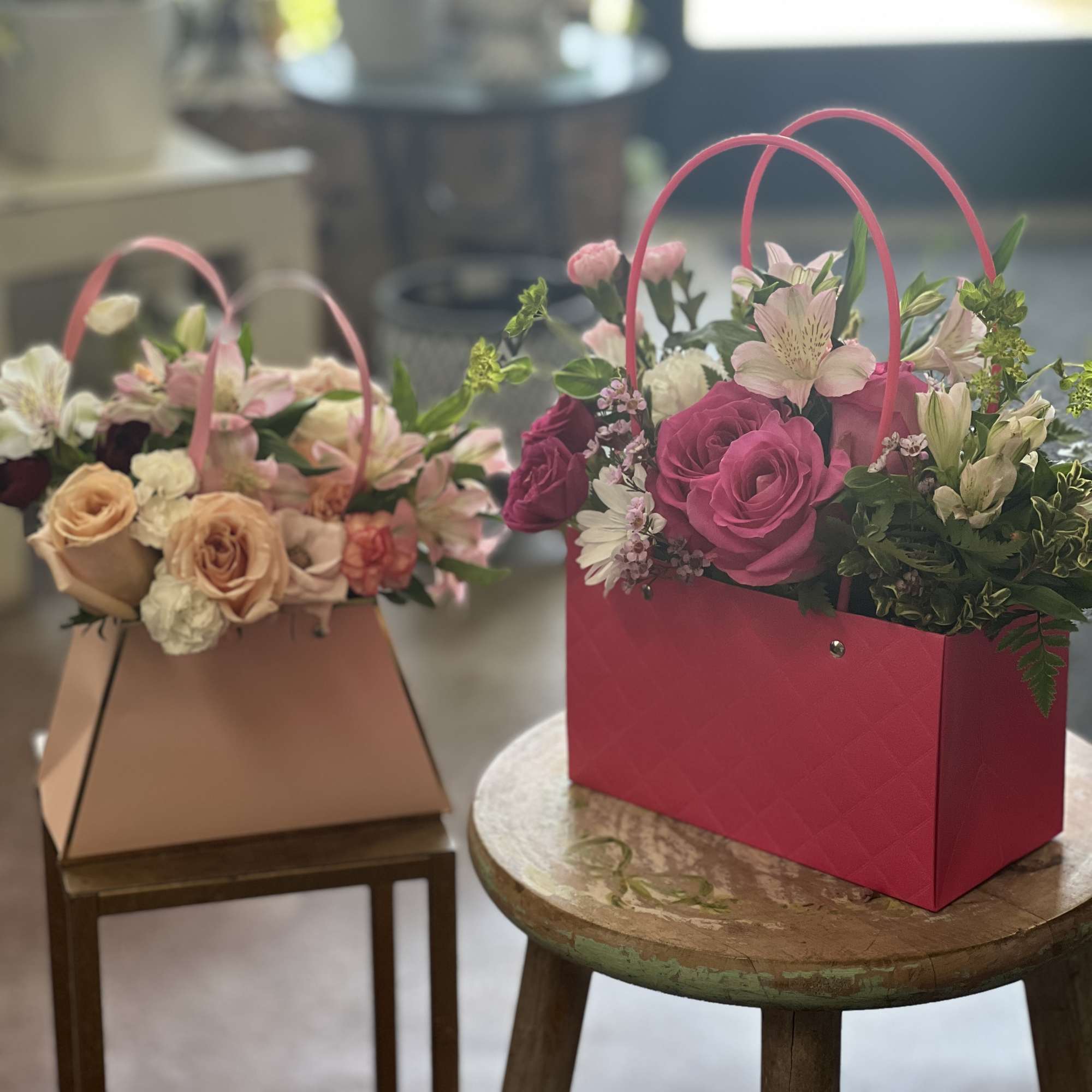 Two flower arrangements in handled gift bags on stools